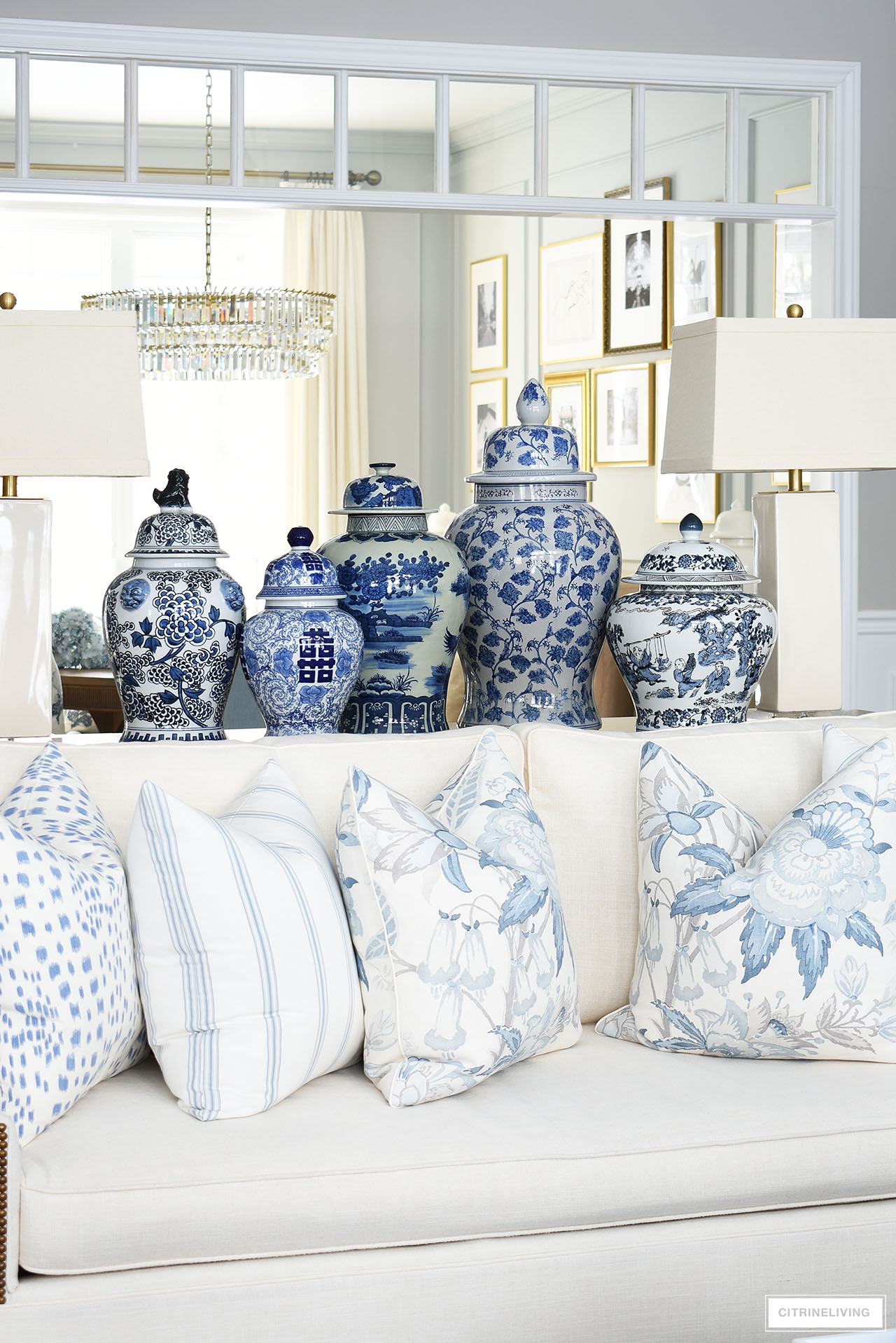 A beautiful collection of large blue and white ginger jars styled on a console behind designer throw pillows in floral, stripe and animal print patterns in blue and white.