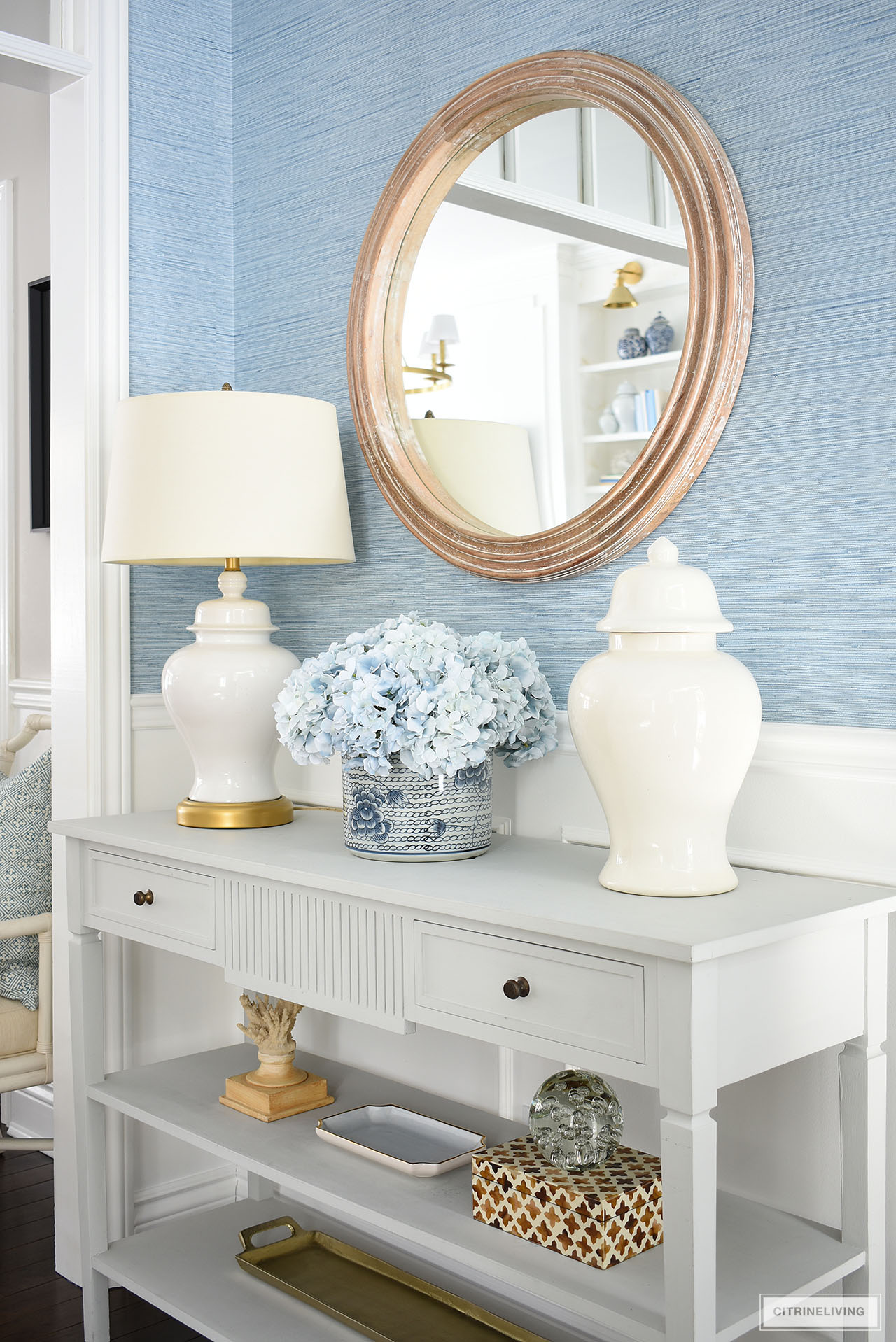 Spring decor styled on a beautiful console table with blue and white planter and blue hydrangeas, white ginger jar and lamp and neutral toned accessories.