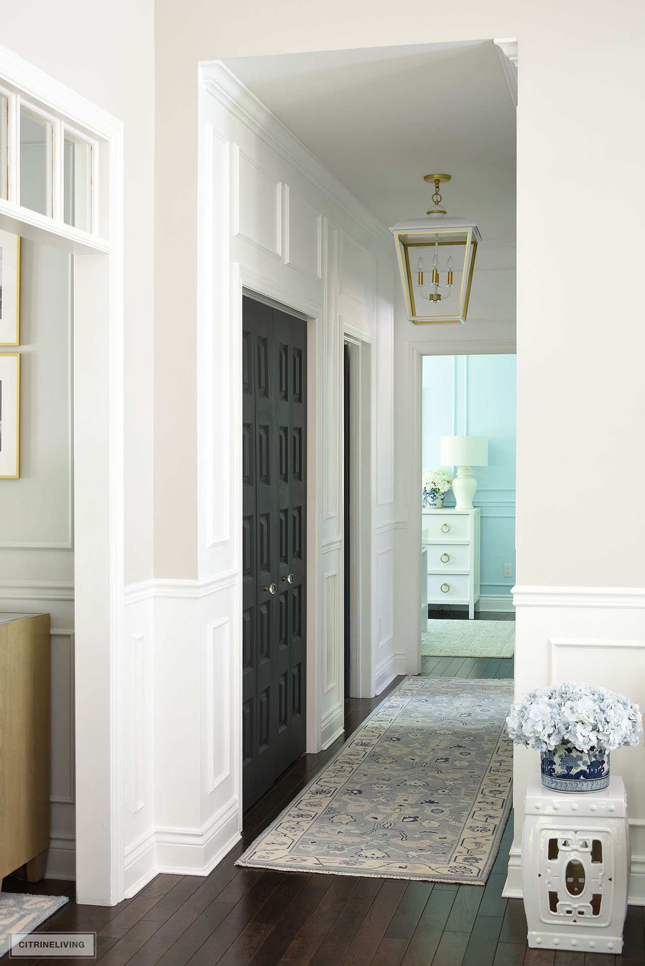 A beautiful hallway makeover featuring white painted walls with moldings, a large white and gold lantern pendant light and a beautiful oushak runner.