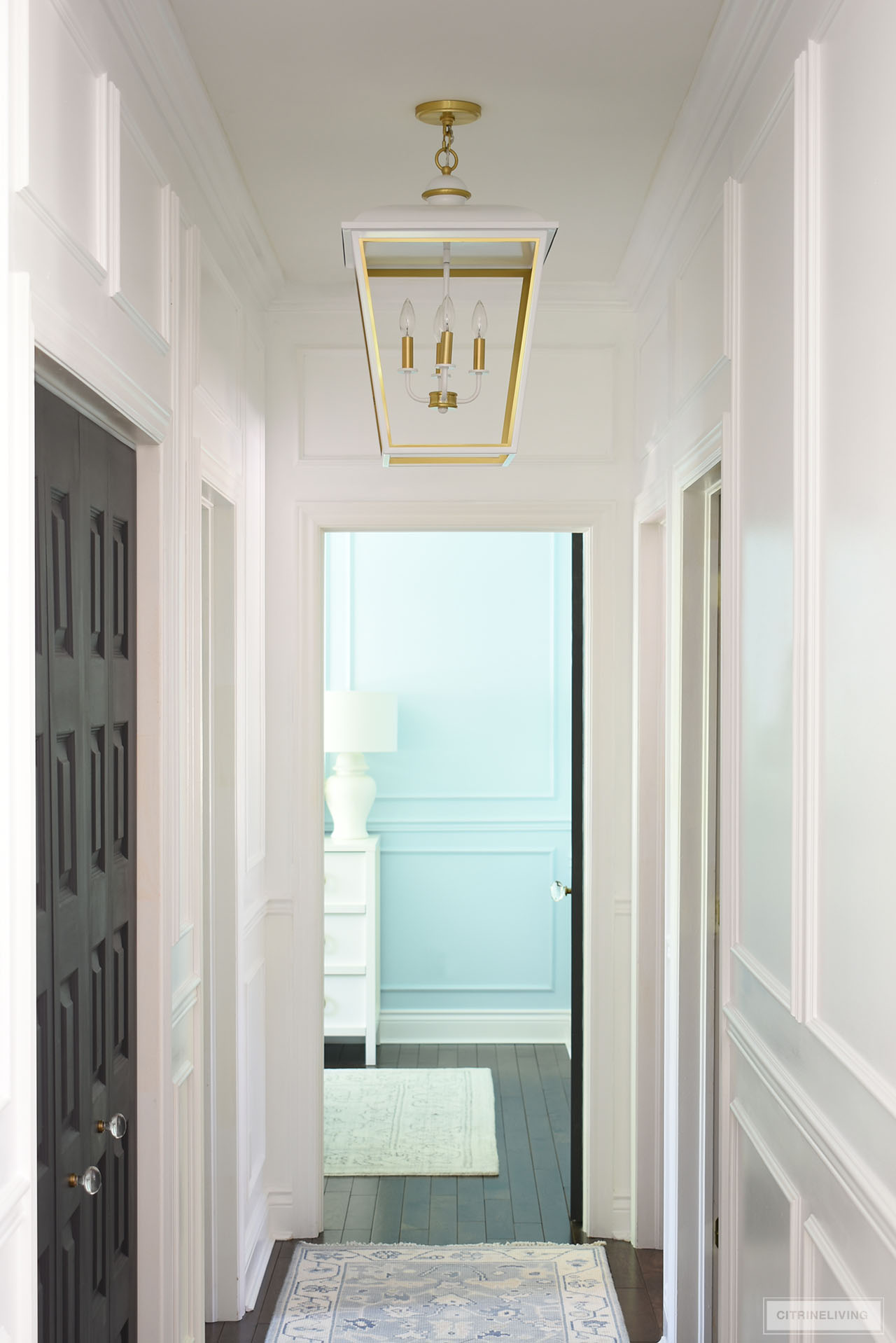 An oversized lantern pendant light in white and gold hangs in a small hallway painted Ultra Pure White by Behr.