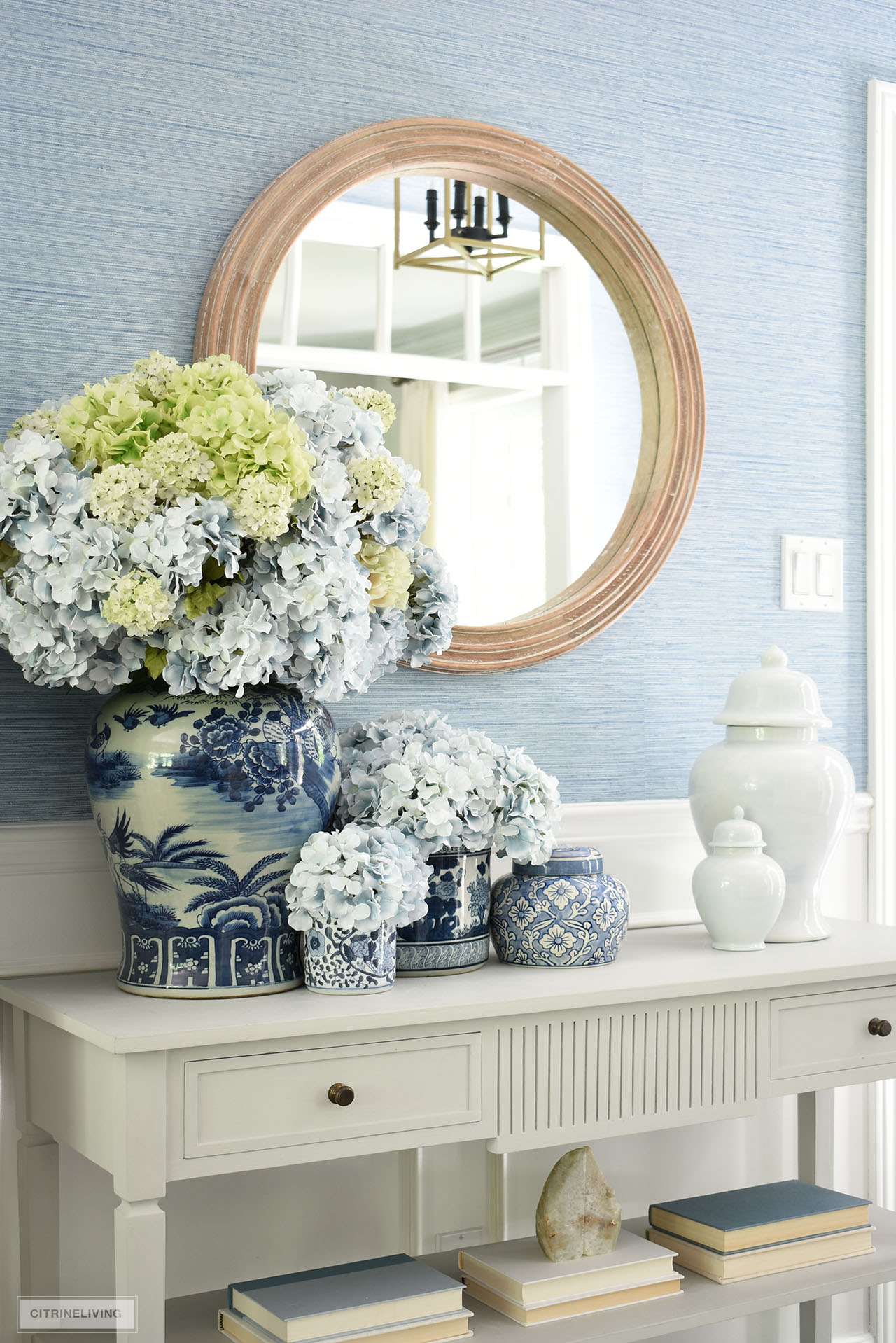 Blue and white ginger jars, containers and vases styled in a beautiful grouping in this summer entryway makes a chic statement arranged with beautiful blue and green hydrangeas.