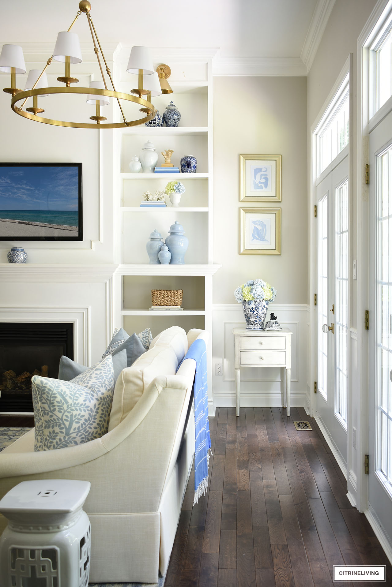 Living room bookshelves styled with blue and white ginger jars, baskets, hydrangeas and coastal accents for summer.