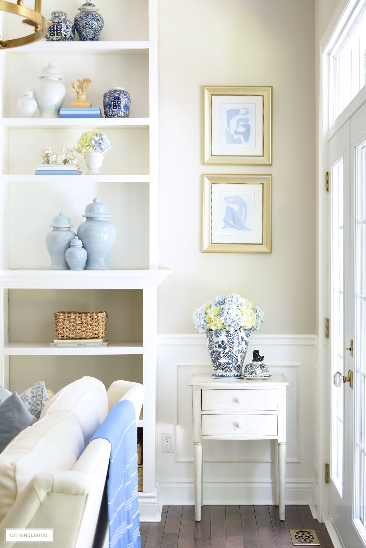 Living room bookshelves decorated for summer with coastal touches, and a combinations of blue and white chinoiserie and solid ginger jars.
