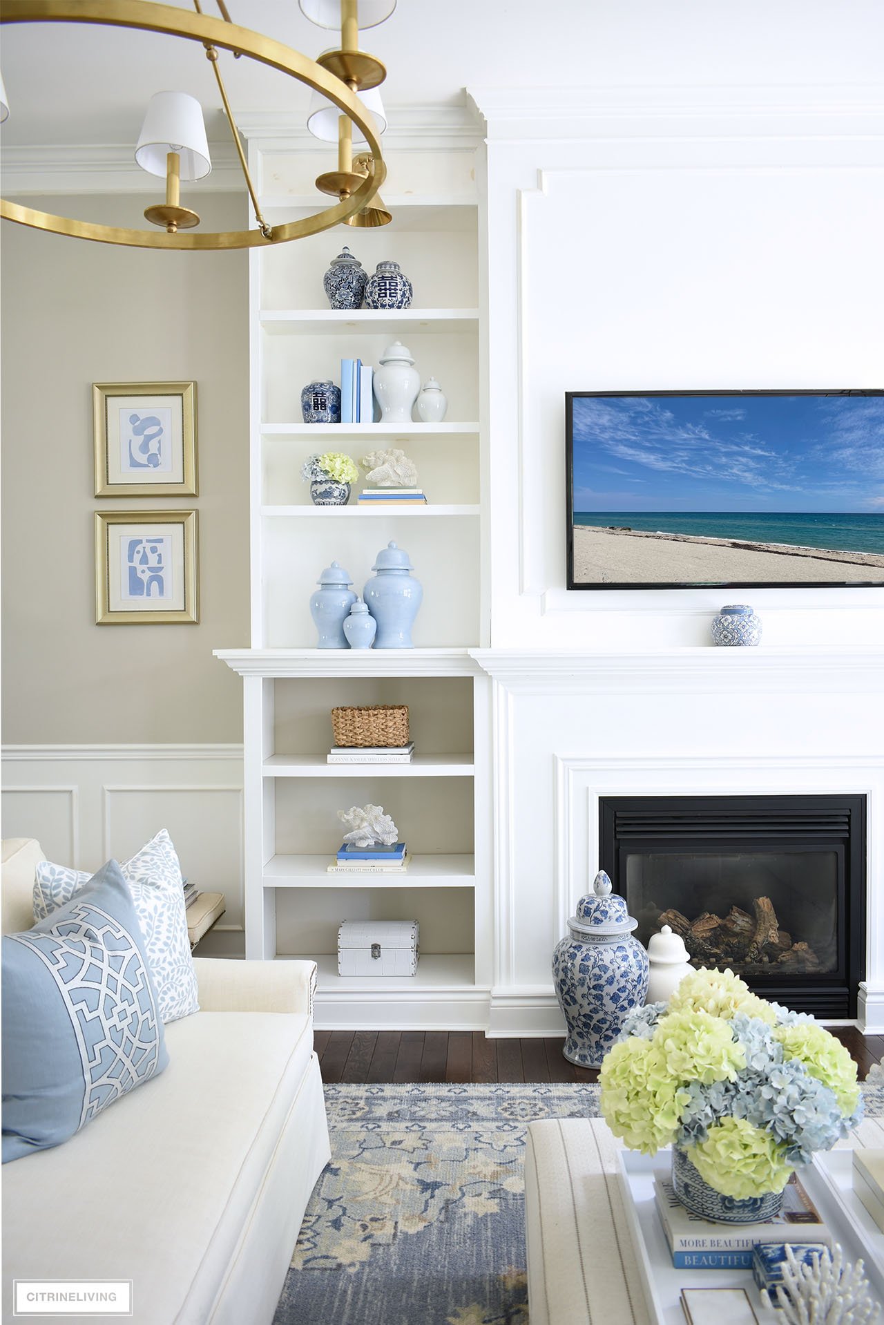 Beautifully styled bookshelves with a mix of blue and white chinoiserie, solid ginger jars in different shades of blue, woven baskets, color blocked books and coastal accents.