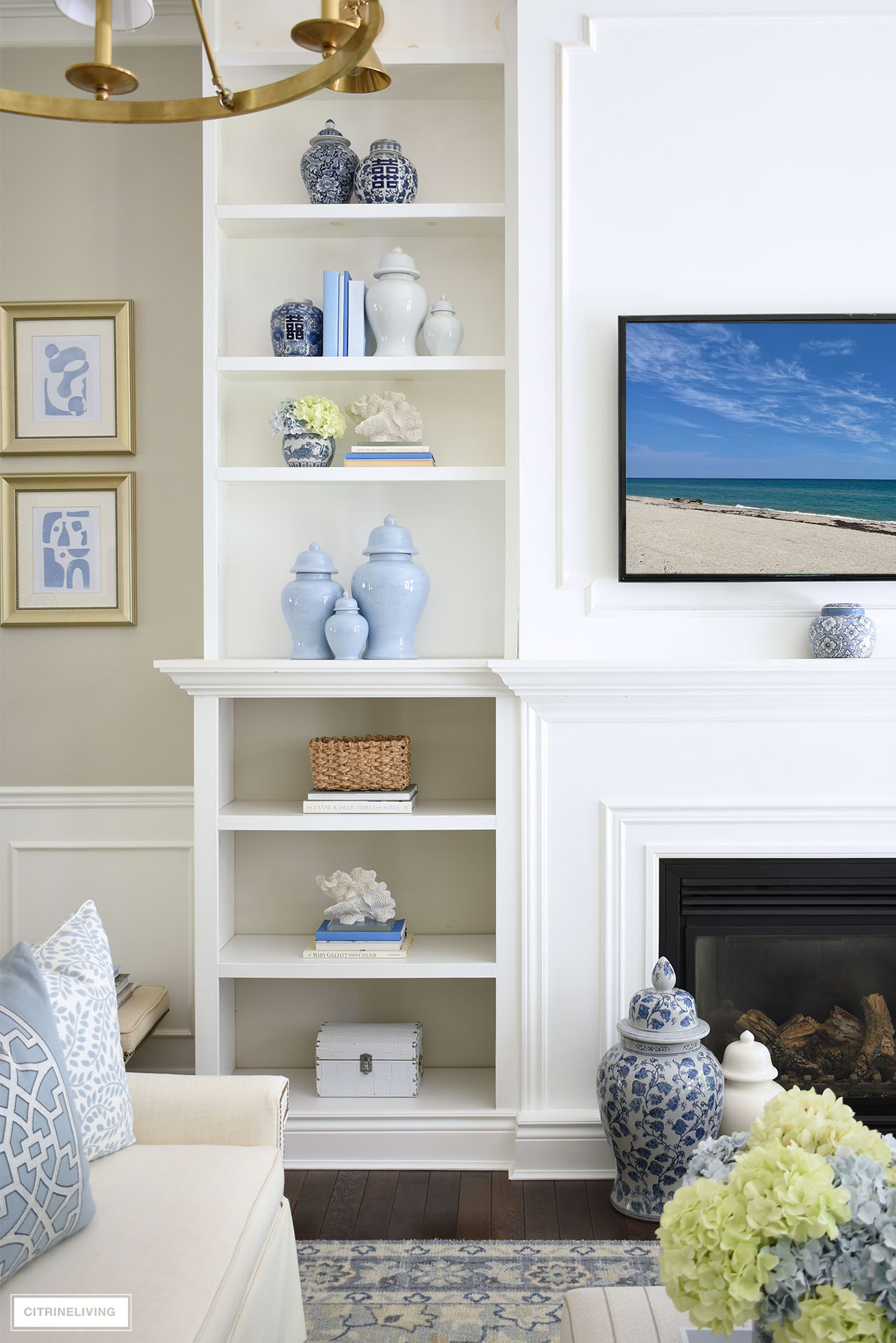 Bookshelves styled for summer with ginger jars, baskets, books, coastal accents and faux hydrangeas.