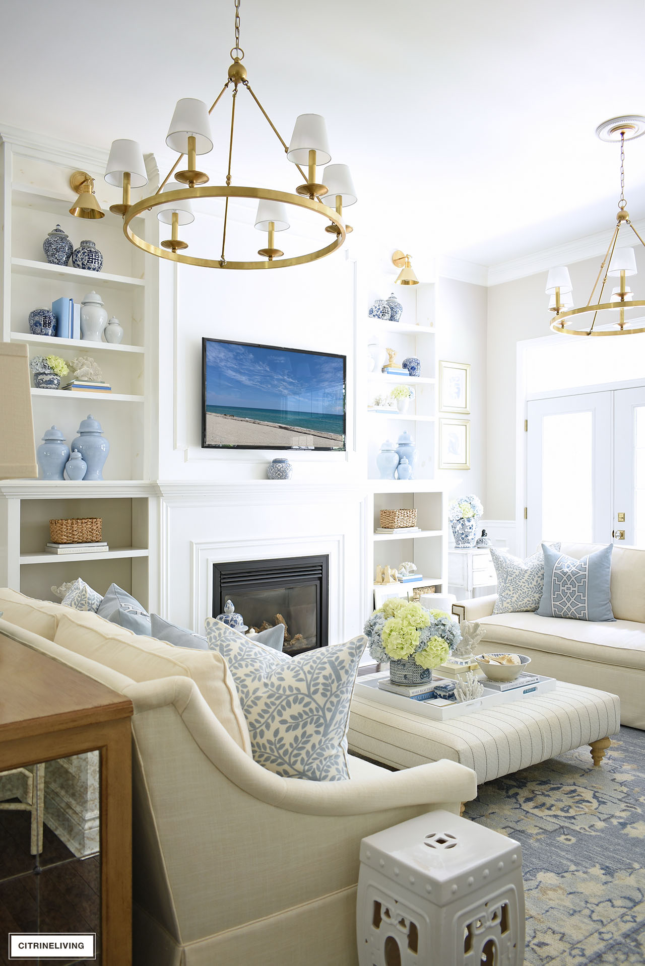 Living room with beautiful ceiling height bookshelves decorated for summer with a soft blue and white color palette, ginger jars, baskets, and blue and green hydrangeas.