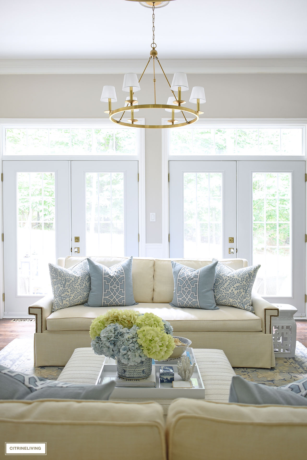 Beautiful living room with white sofa, blue and white decor, brass chandelier and double french doors with transoms.