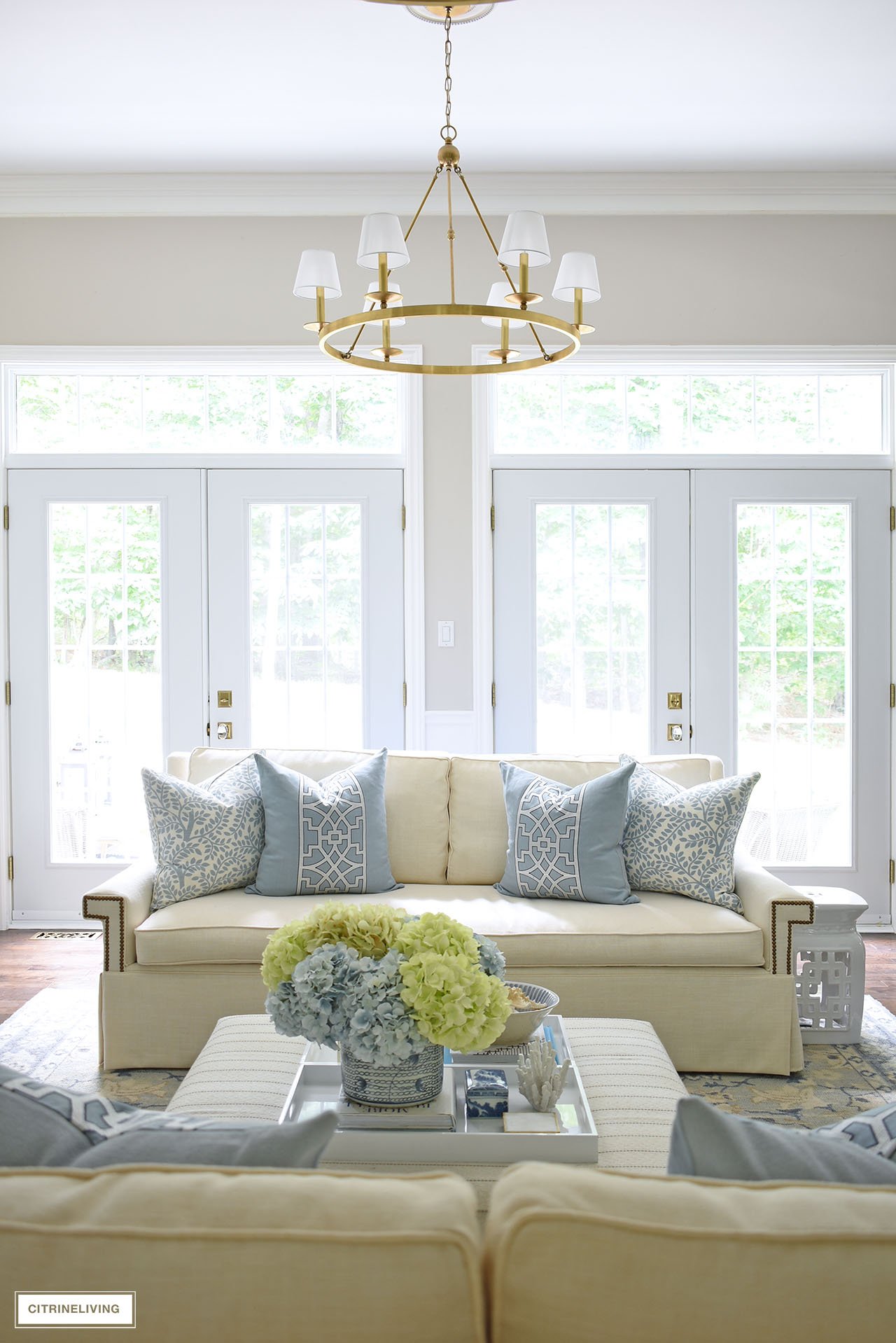 Beautiful living room with white sofa, blue and white decor, brass chandelier and double french doors with transoms.