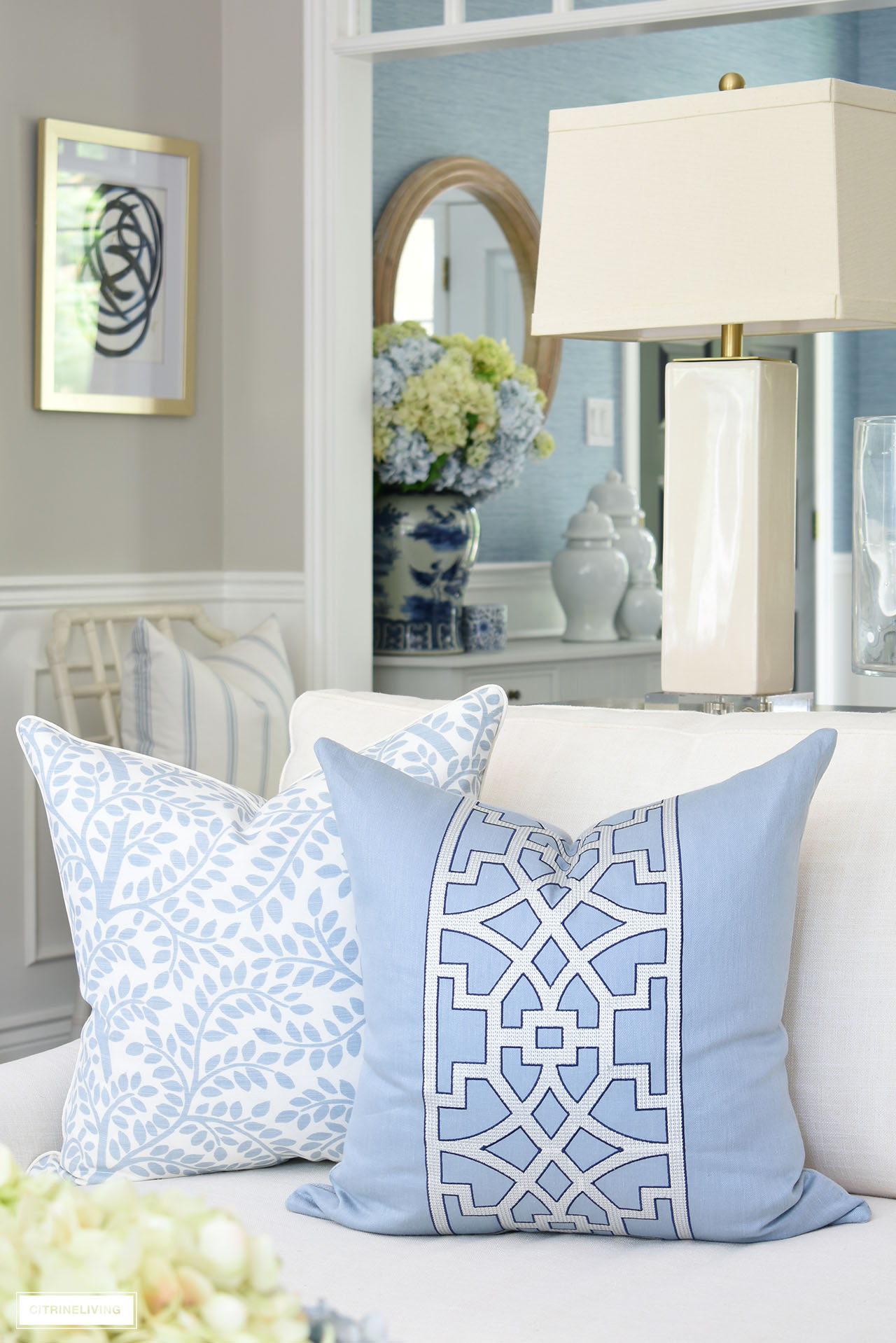 Gorgeous designer pillows in blue and white, one featuring a wide trellis detail on the front in white on a light blue ground, outlined in navy blue, while the other has a light blue allover leaf print on a white linen ground.