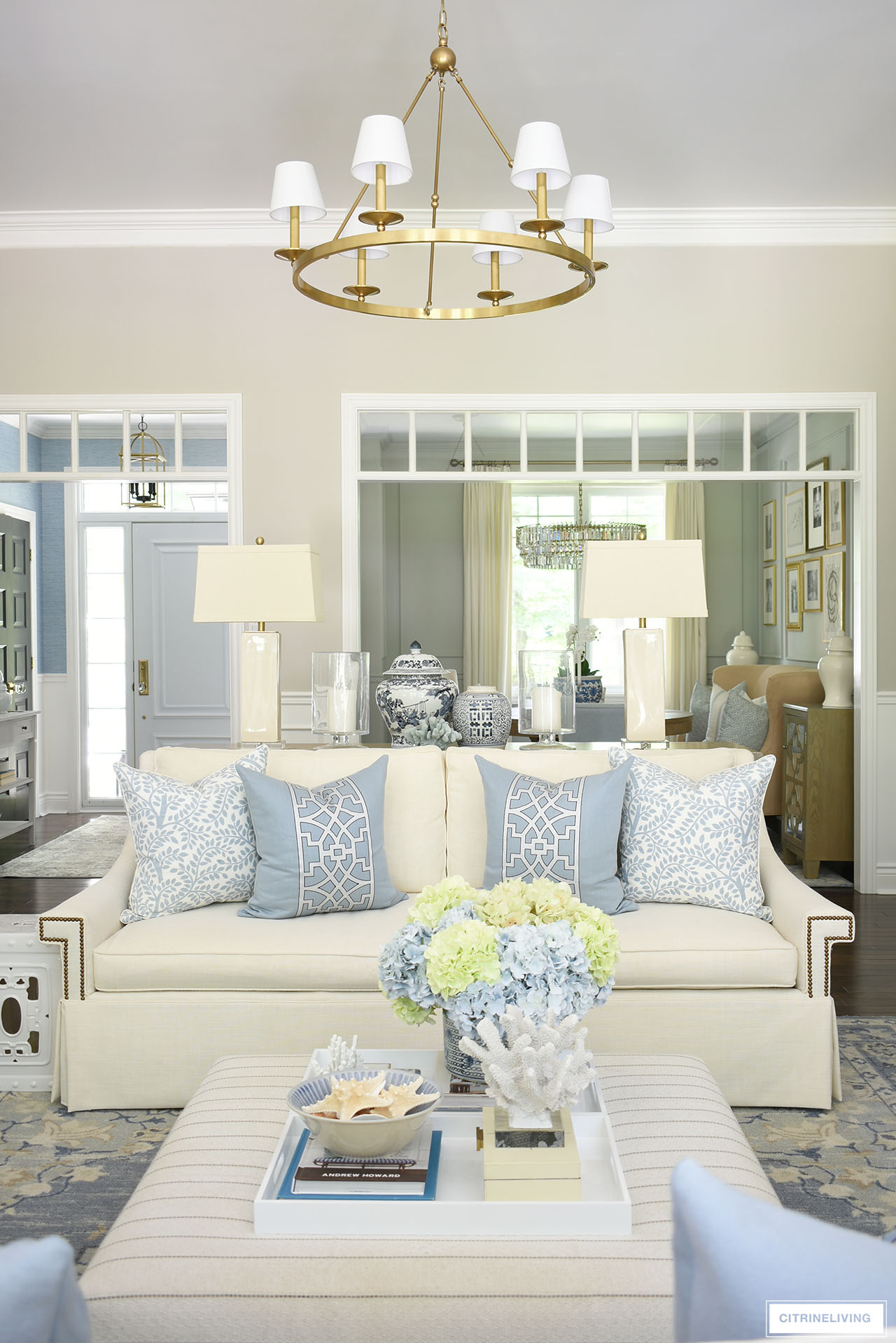Living room styled for summer with an elegant light blue and white color palette, designer pillows, blue and green hydrangeas and coastal accents.