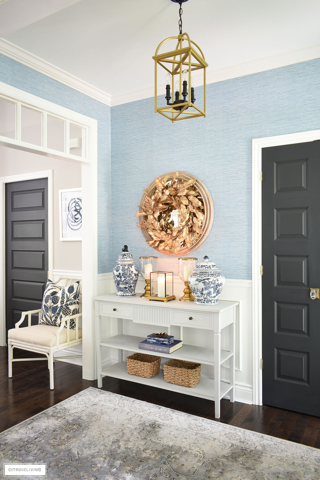 Fall entryway table decorated with a gorgeous gold wreath, blue and white ginger jars, gold candleholders, baskets, boxes and books creates an elegant welcome.