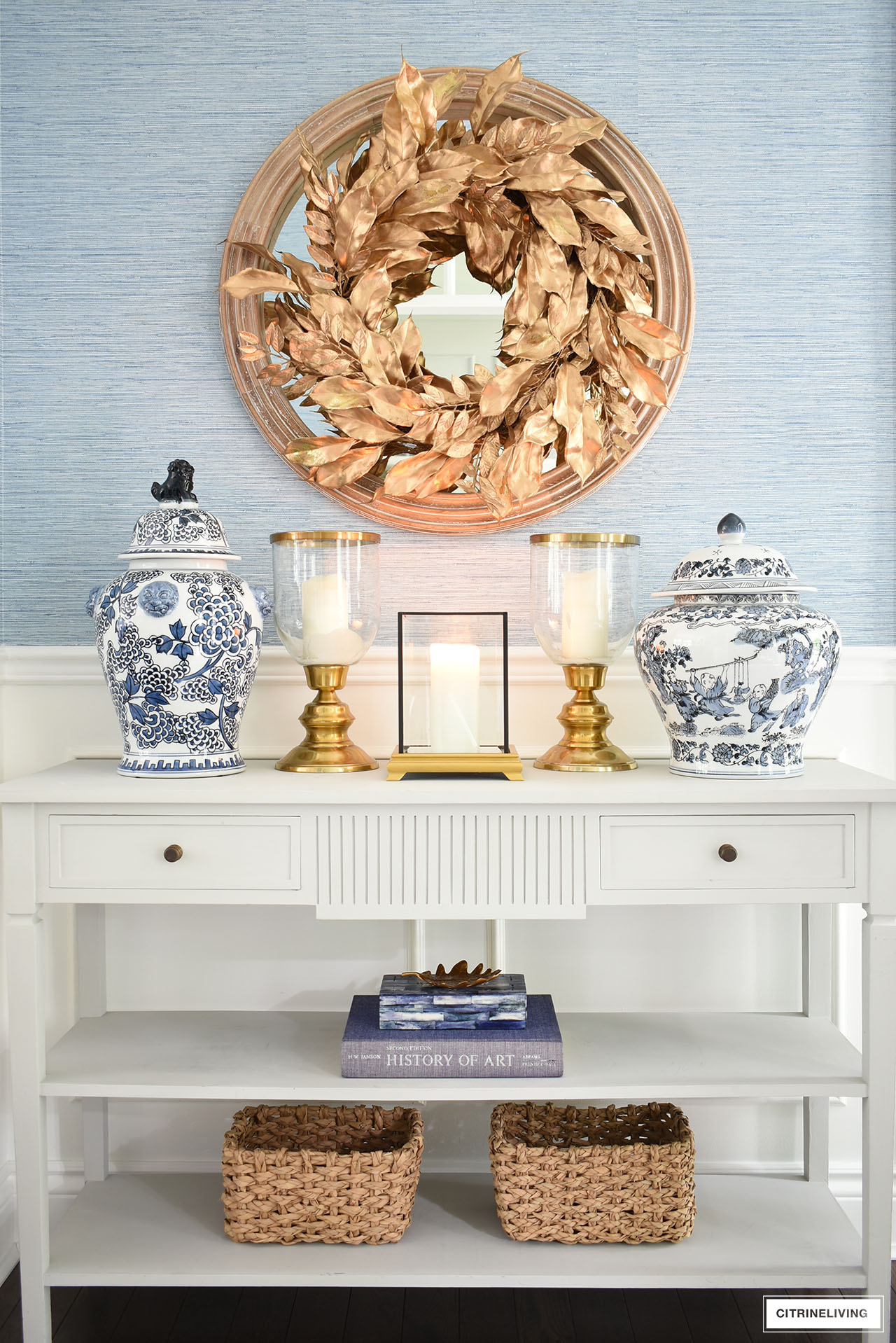 Beautifully styled console table with gold candle holders and ginger jars, styled along with accents - baskets, decorative box and book, finished with a gorgeous god wreath above.