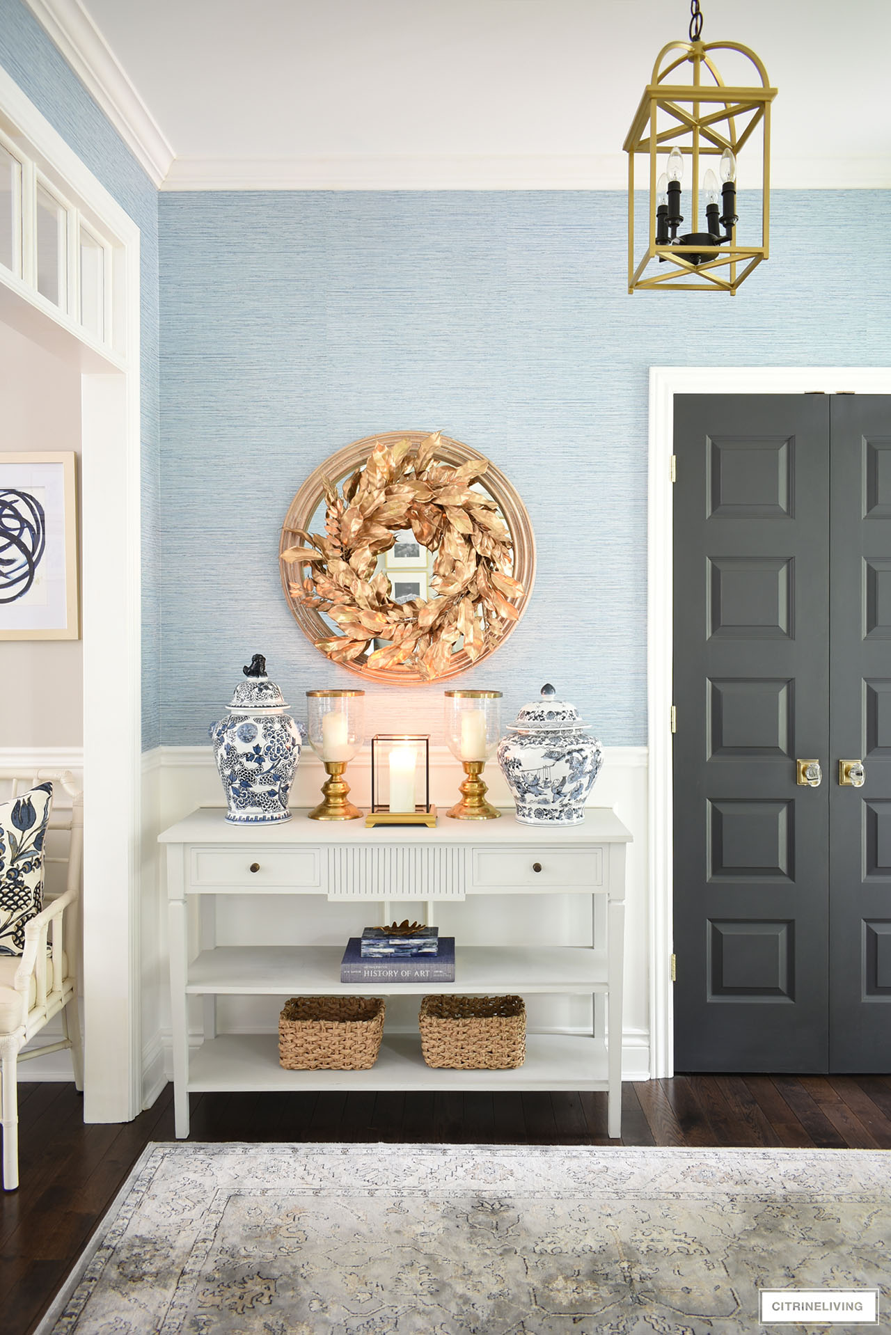 A gorgeous gold wreath, blue and white ginger jars, gold candleholders, baskets and a simple vignette with a large book, decorative box and a small gold leaf, dresses up a simple and elegant entryway table for fall.