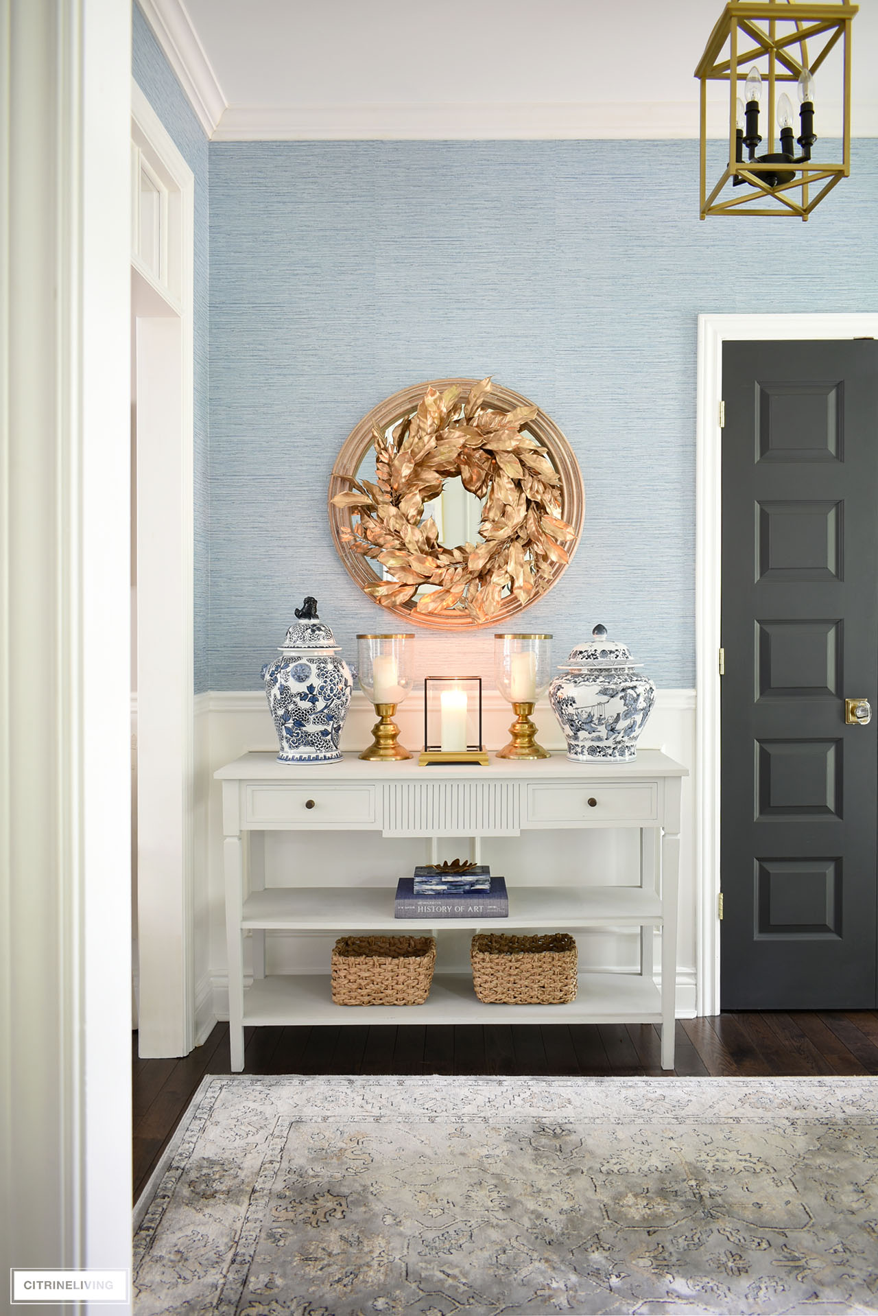 Beautiful fall entryway decor with gold and blue accessories, a beautiful gold wreath, and woven baskets for a timeless and elegant look.
