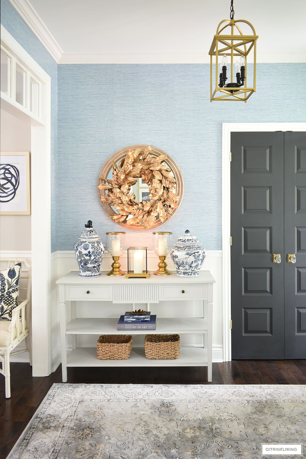 Entryway table decorated for fall with a chic gold wreath, blue and white ginger jars, gold candleholders, baskets, book and box in timeless blue is a simple take on the season.