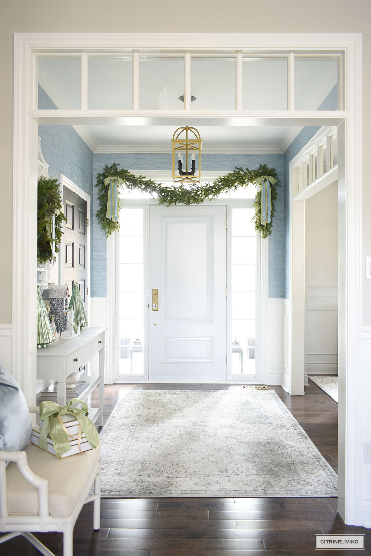 Christmas decor in an elegant entryway, with garland swagged over the front door, embellished with light green and light blue bows on each corner.