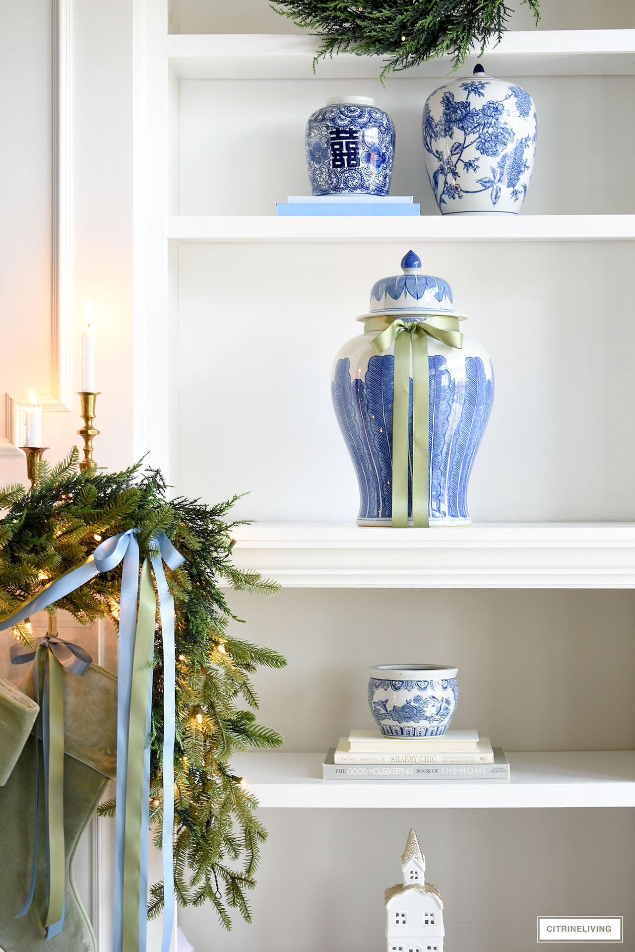 Blue and green decorated bookshelves for Christmas. Ginger jars dressed with ribbon, green garland with ribbon.