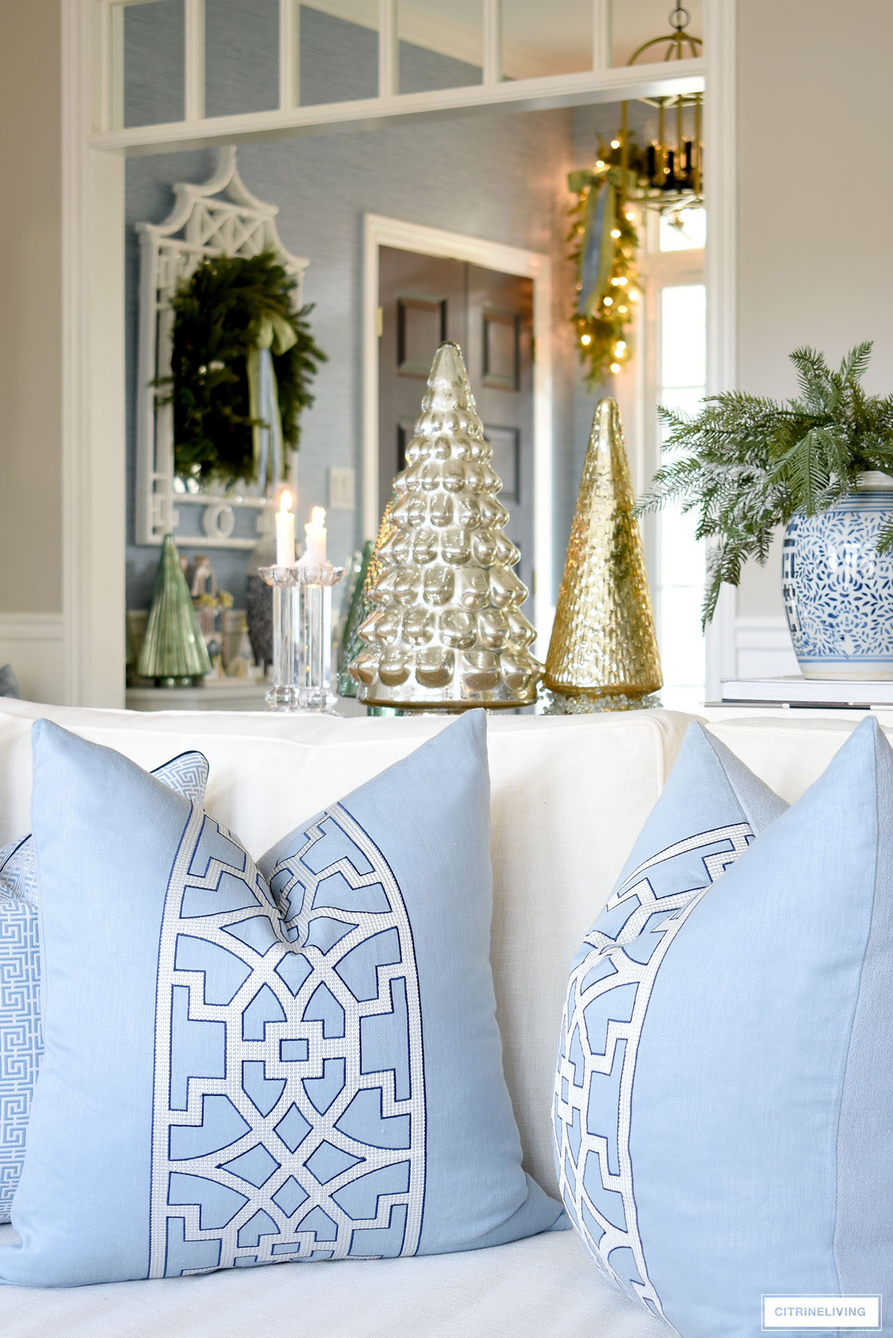 Blue and white throw pillows on a white sofa, Christmas trees in mercury glass and a blue and white ginger jar arranged with holiday greenery.