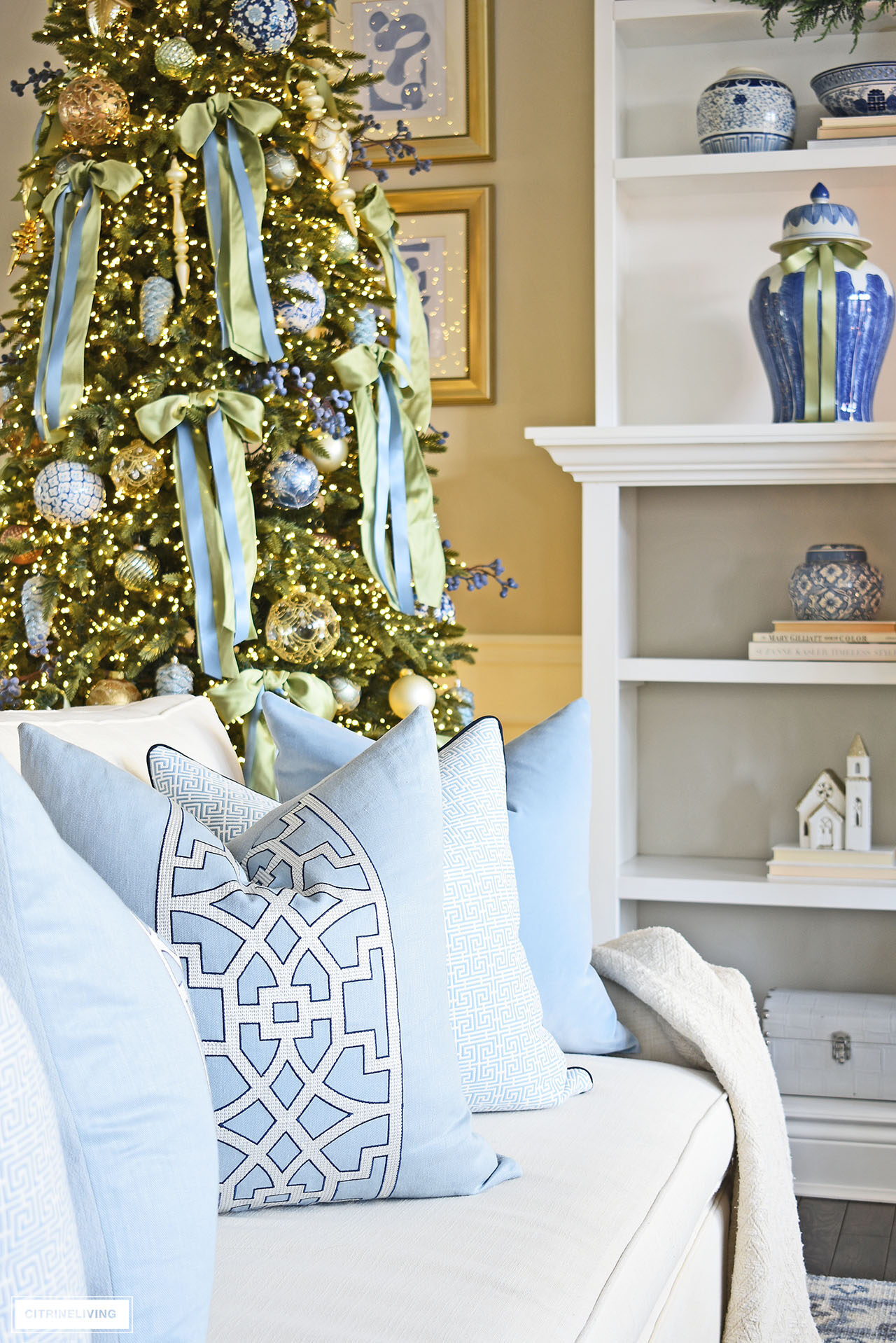 Blue and white throw pillows on a white sofa, Christmas tree decorated with light green and blue bows sits behind.