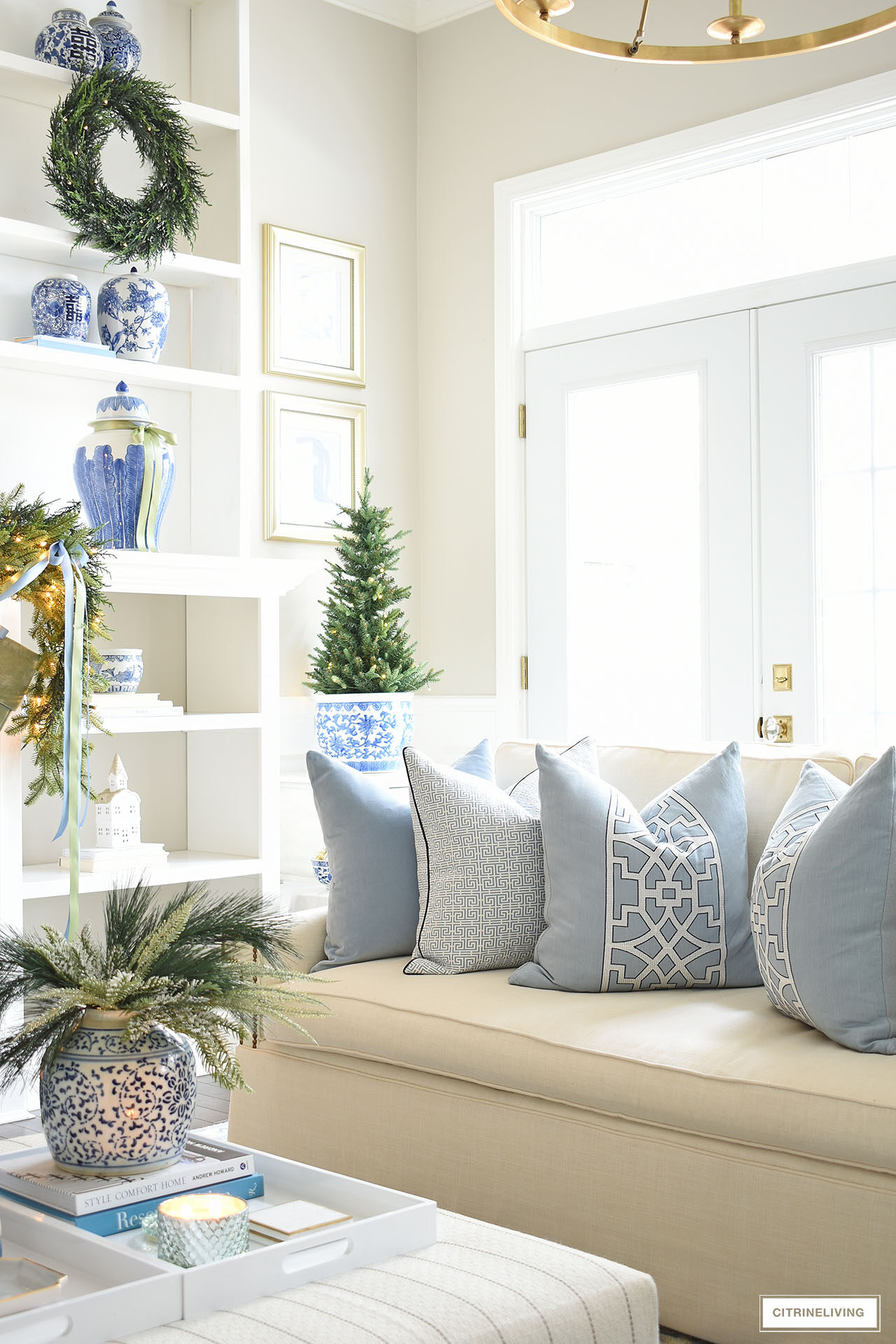 Blue and white throw pillows on a white sofa, Christmas decor around the living room with greenery and blue and white chinoiserie.