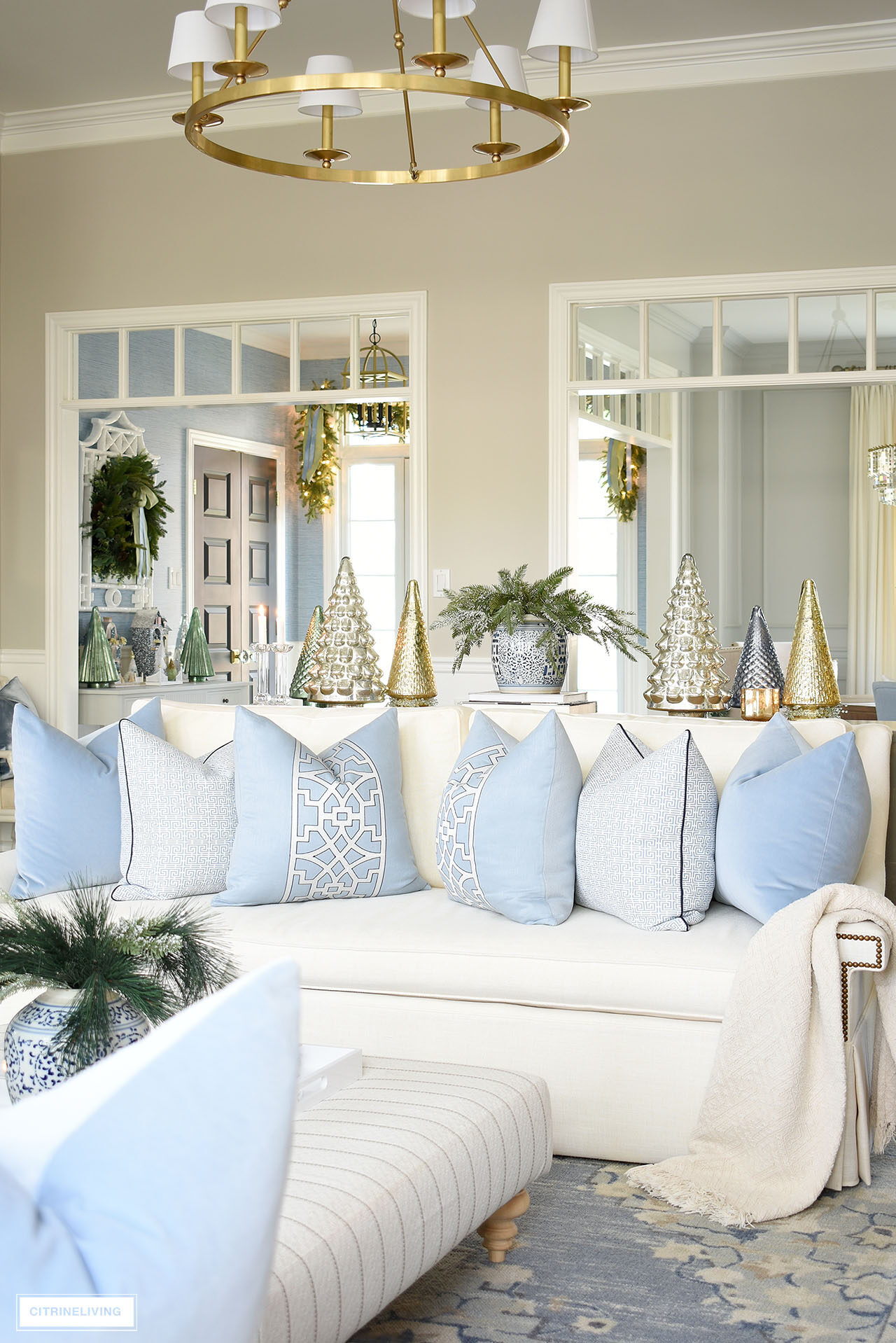 White sofa styled with light blue throw pillows, Christmas decor sits behind on a table. 