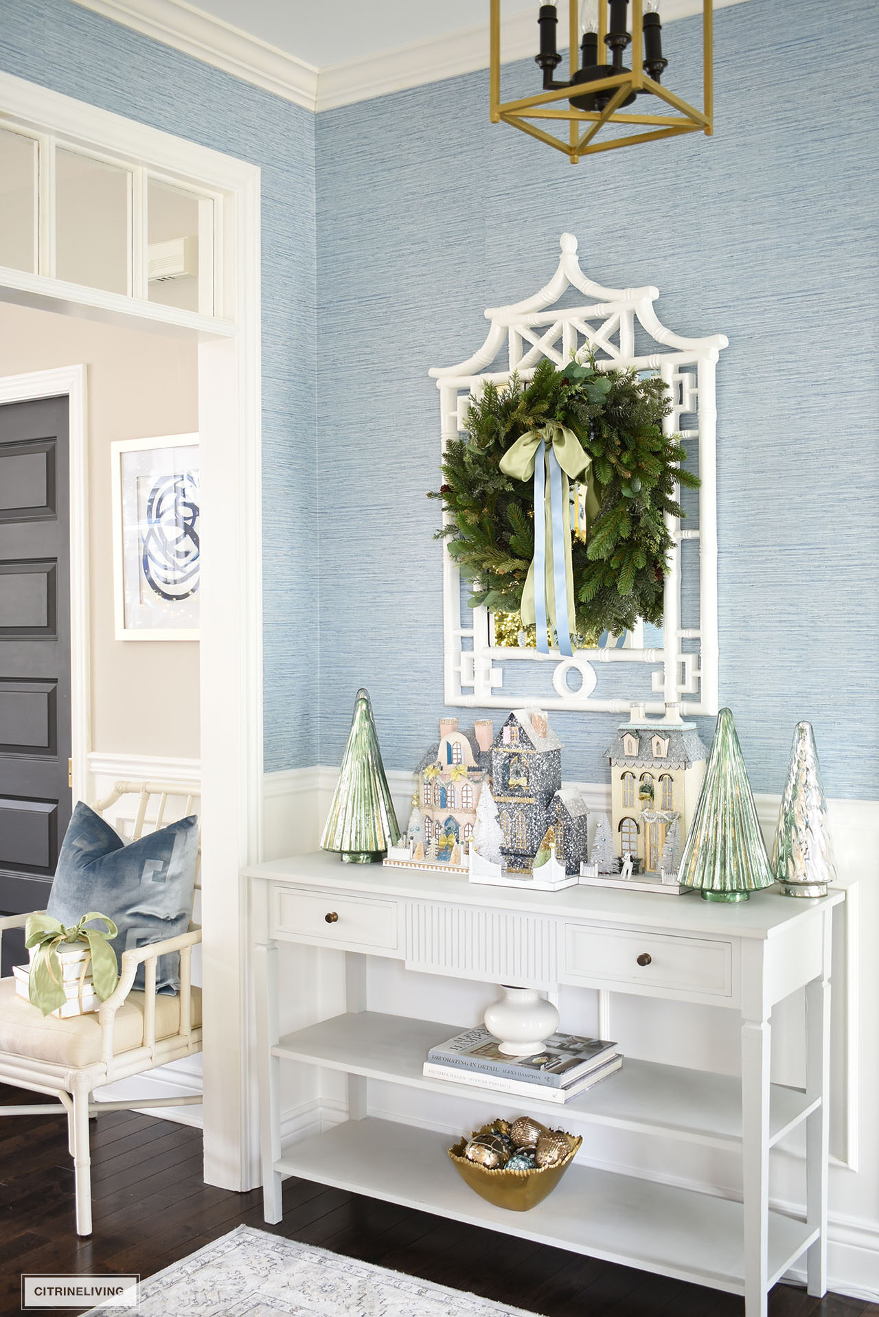 An elegant Christmas display on an entryway console table - decorated with Christmas houses and mercury glass Christmas trees.