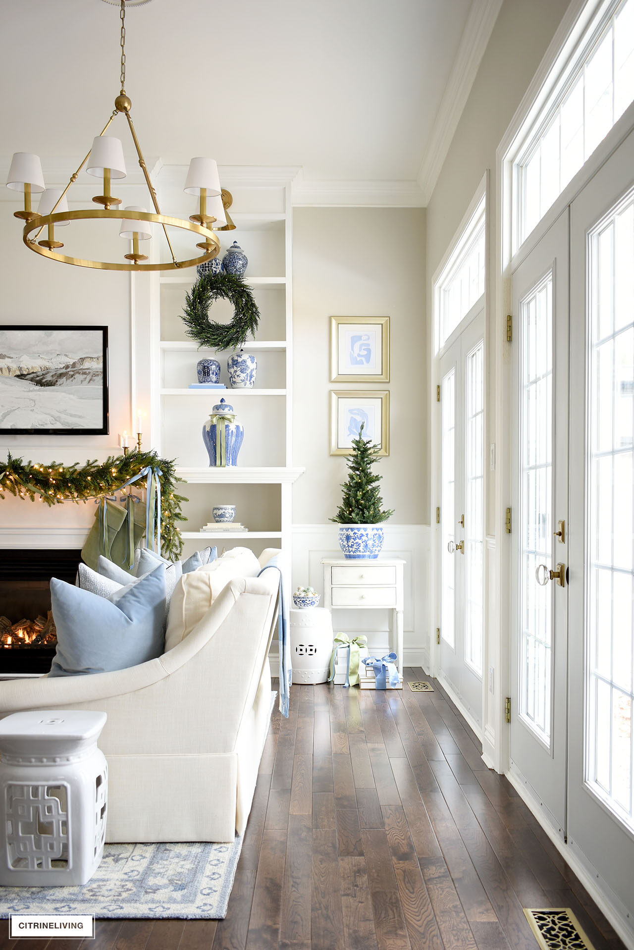 Living room shelves decorated for Christmas with greenery, blue and white chinoiserie accents and light green velvet stockings.