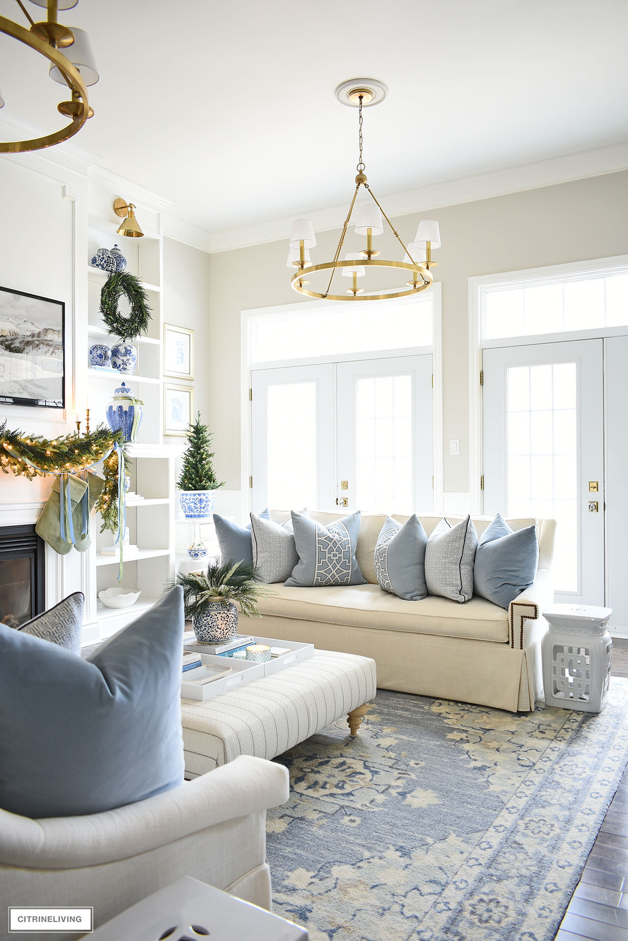 Living room decorated for Christmas with pretty greenery, a white sofa is styled with blue and white pillows.