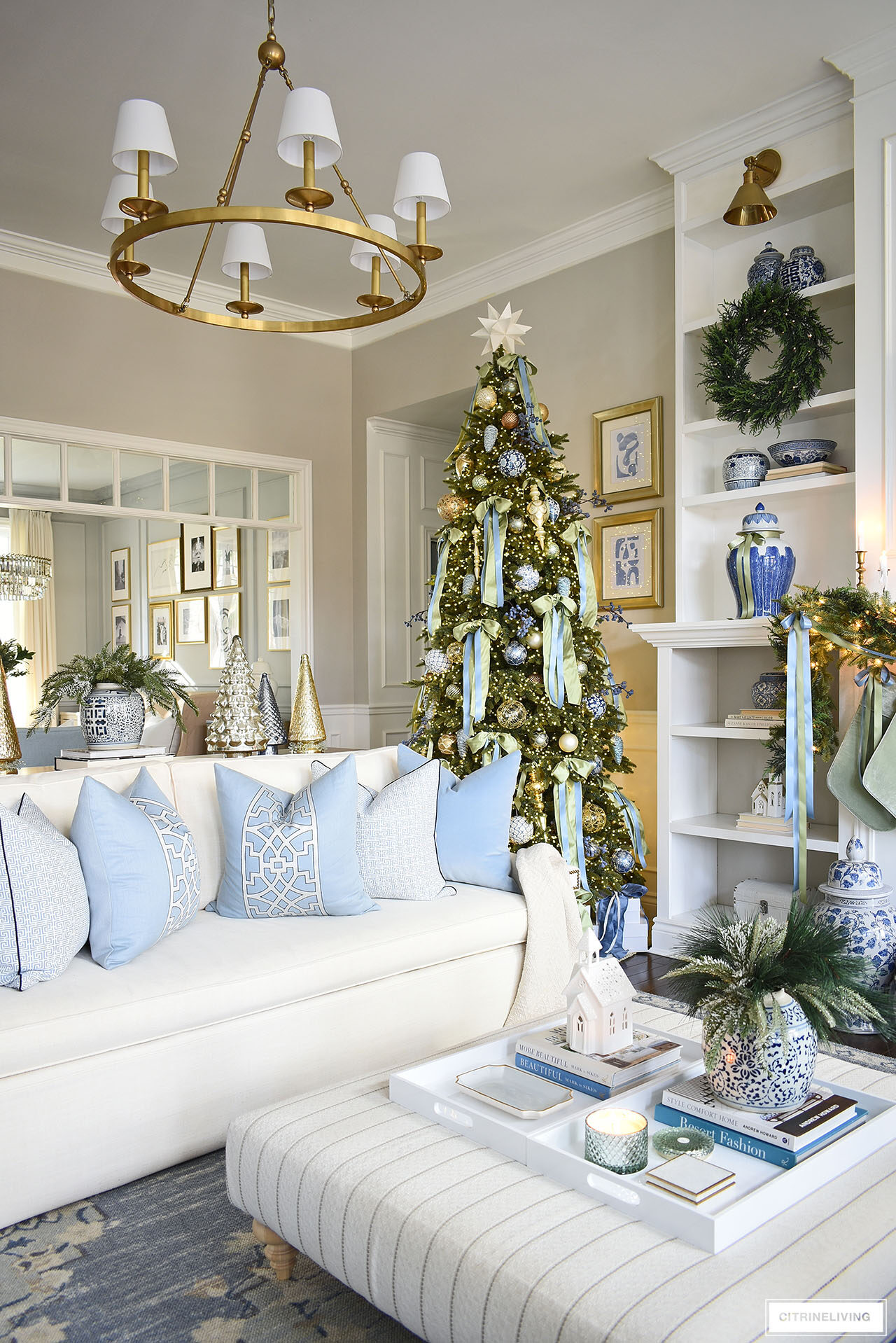 A corner of a living room with a Christmas tree decorated in light green and blue bows, a white sofa is styled with blue and white pillows.