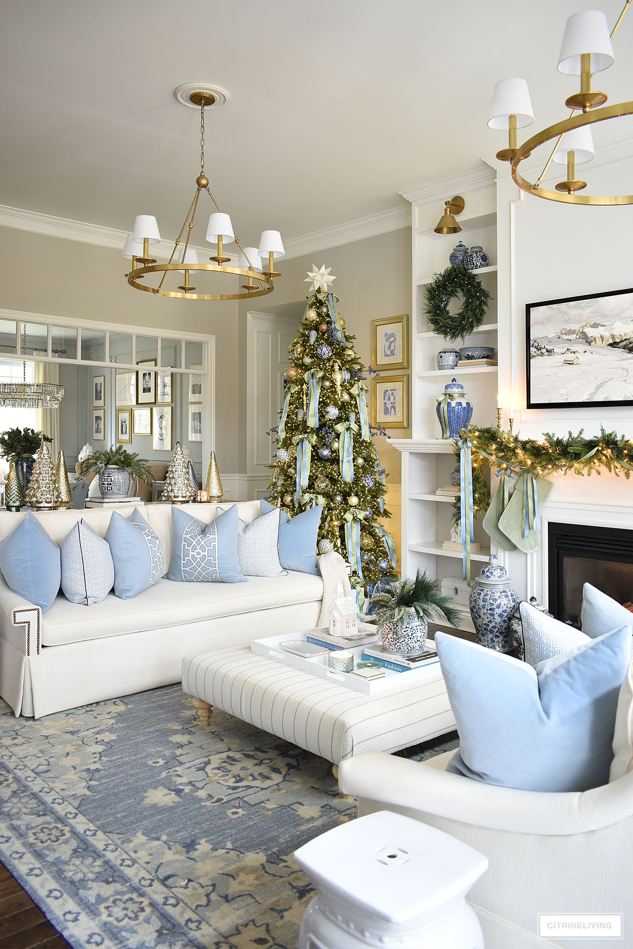 Christmas living room decorated in blue and green with green garland and ribbons on the mantel. Blue and white chinoiserie decor is styled throughout the room.