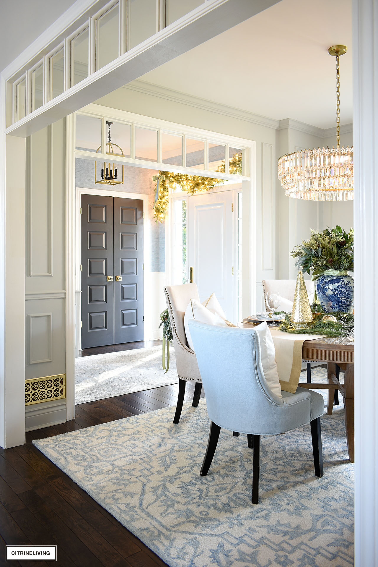 View of a dining room and entryway decorated for Christmas with elegant greenery accents and ribbon