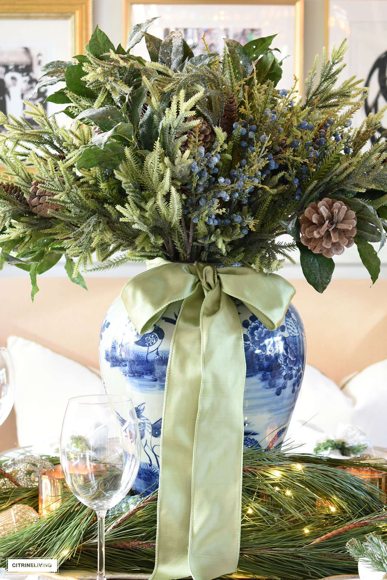 Holiday arrangement with greenery, a blue and white ginger jar and sage green ribbon tied in a bow
