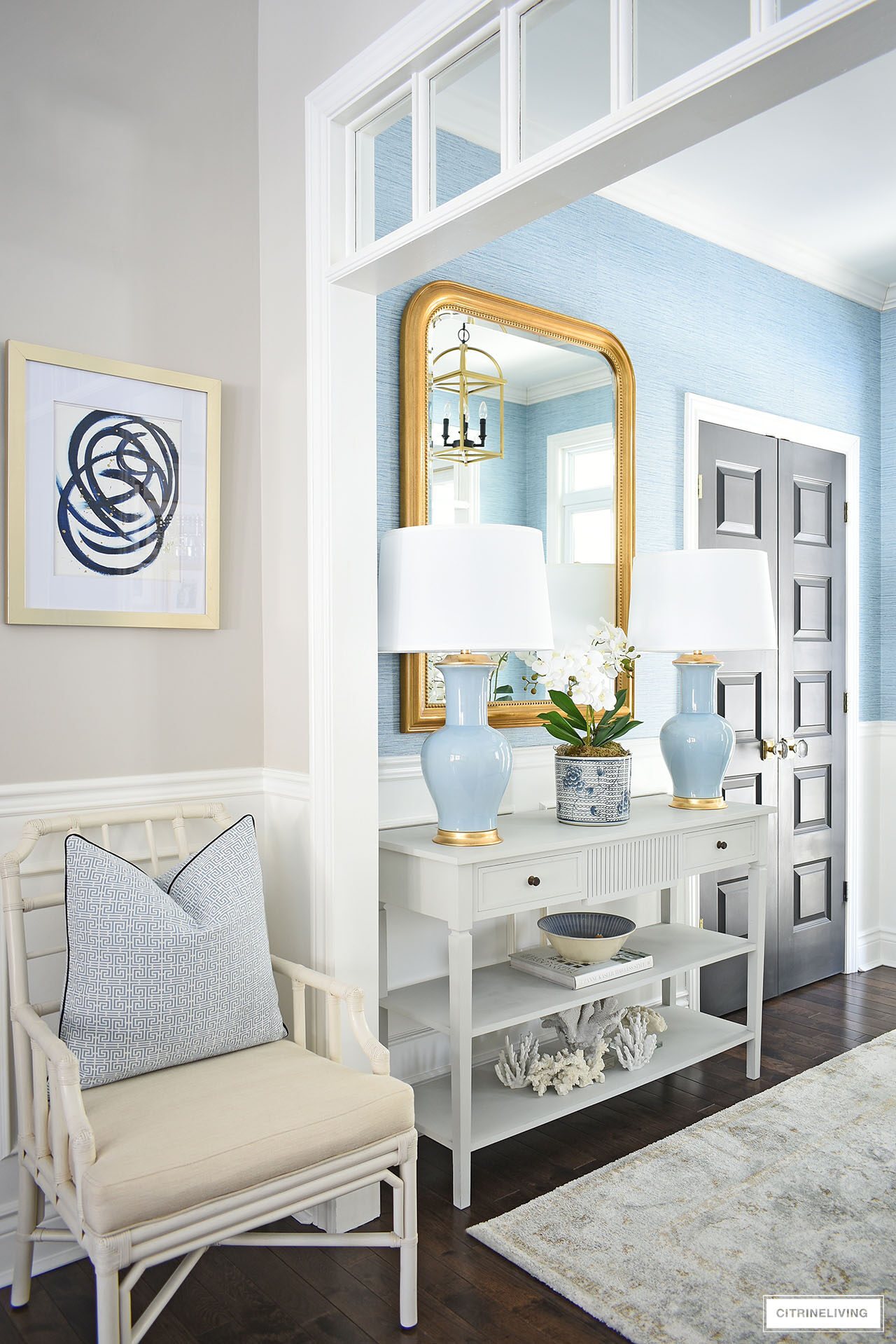Entryway decorated for spring with blue lamps, large gold statement mirror and a soft muted rug