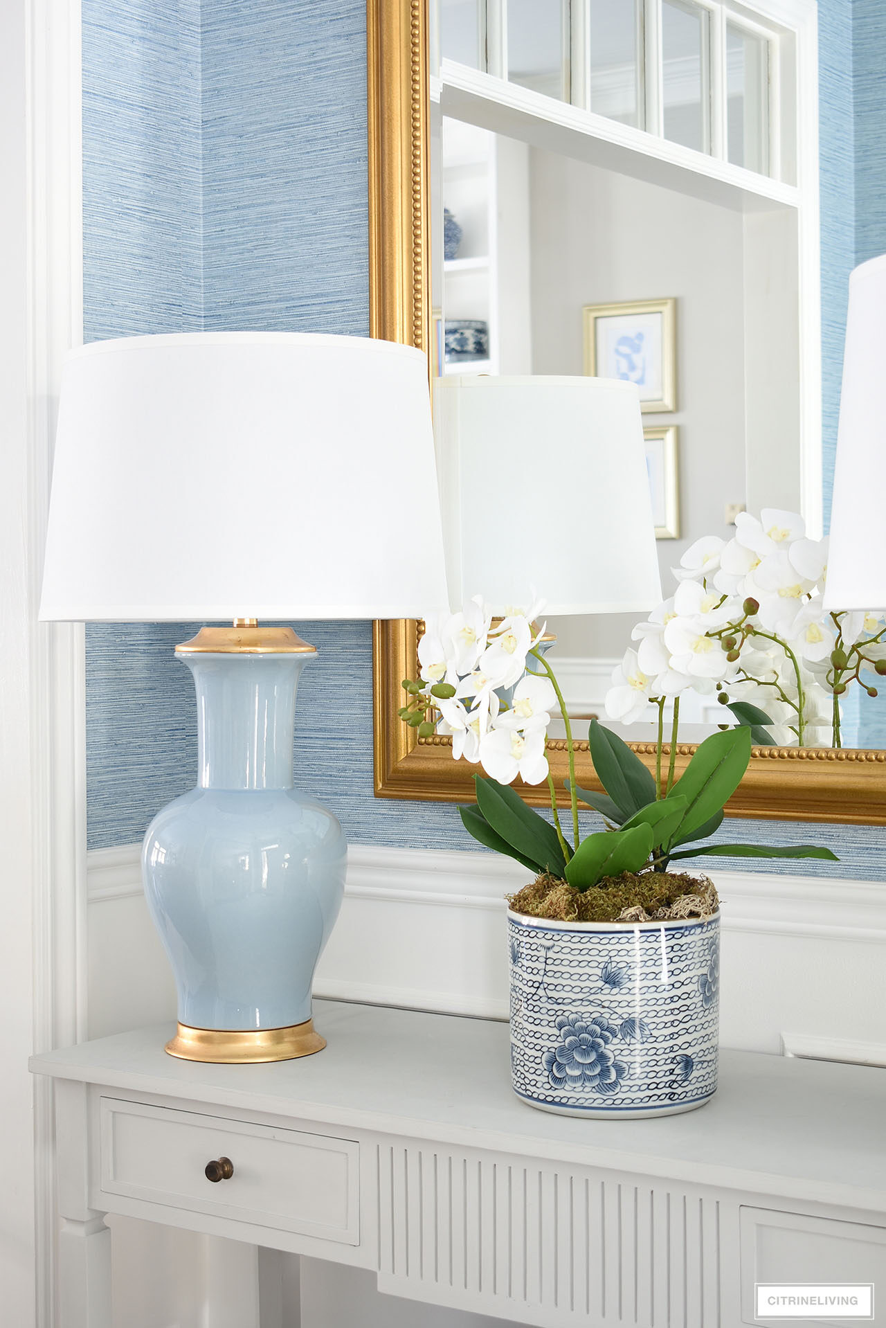 Detail of spring styling featuring a faux orchid arrangement and blue lamp with gold accents.