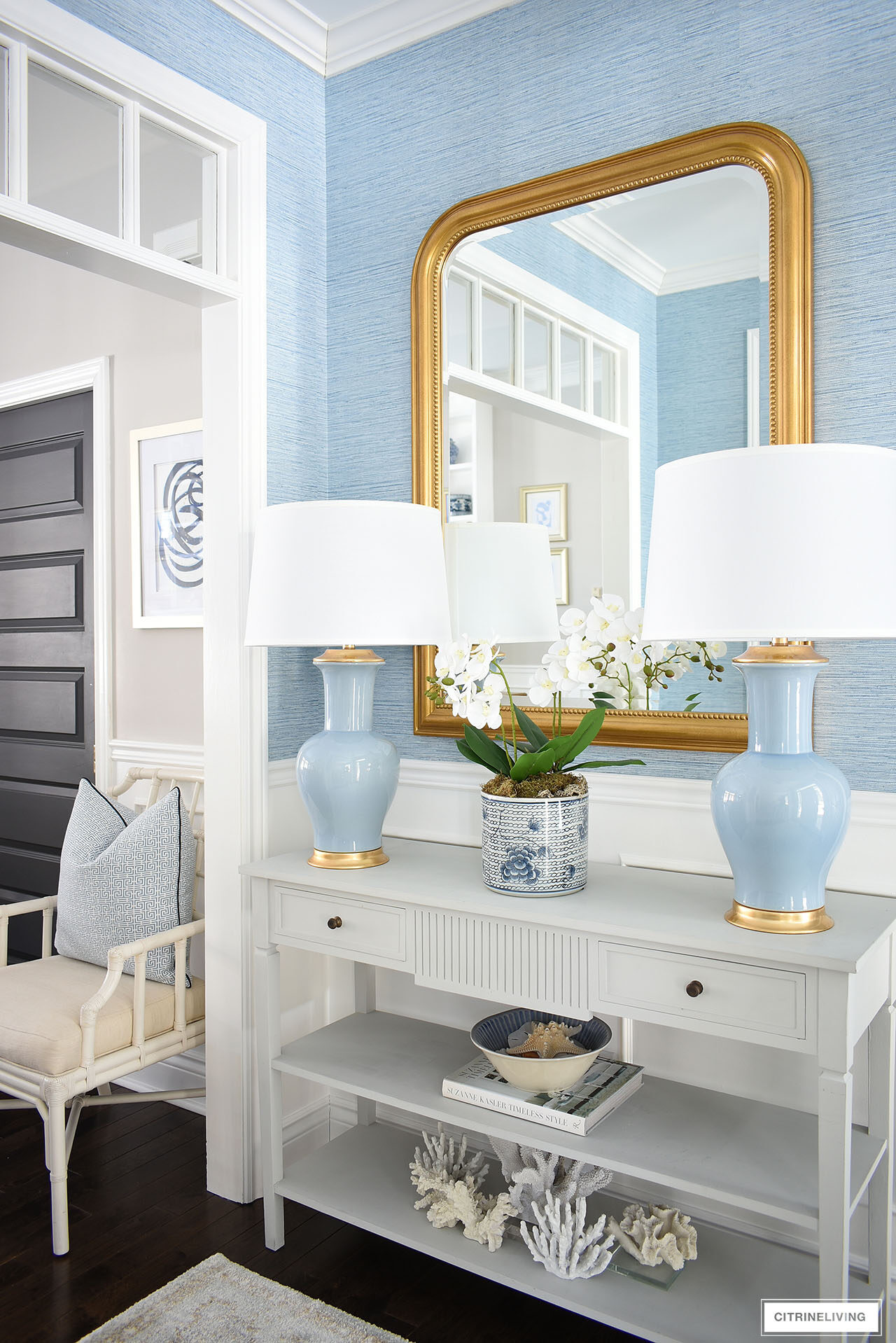 Entryway decorated for spring featuring a pair of blue lamps, large gold statement mirror and a soft muted rug, with faux blue grasscloth wallpaper