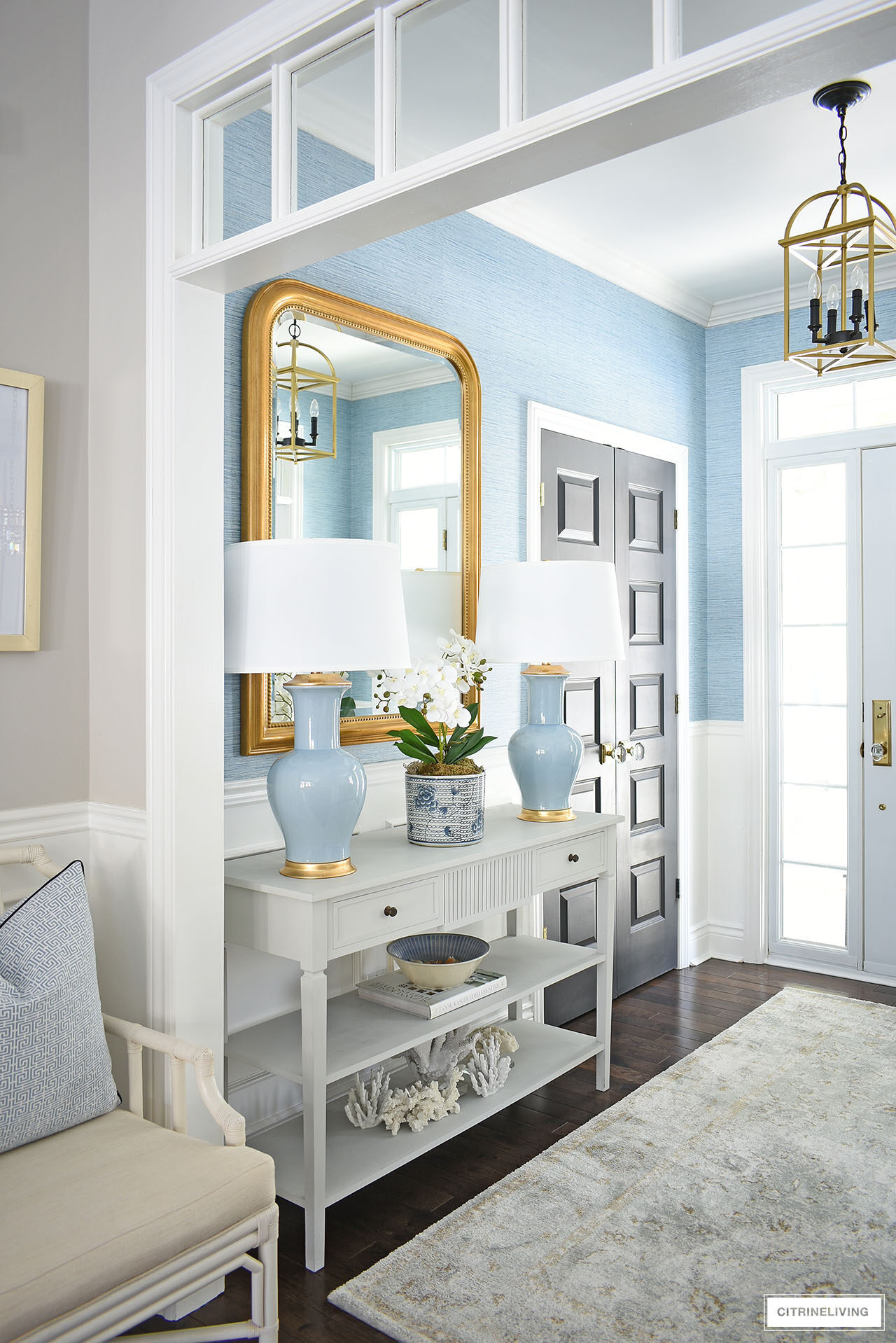 Elegant entryway decorated for spring featuring a pair of blue lamps, large gold statement mirror and a soft muted rug
