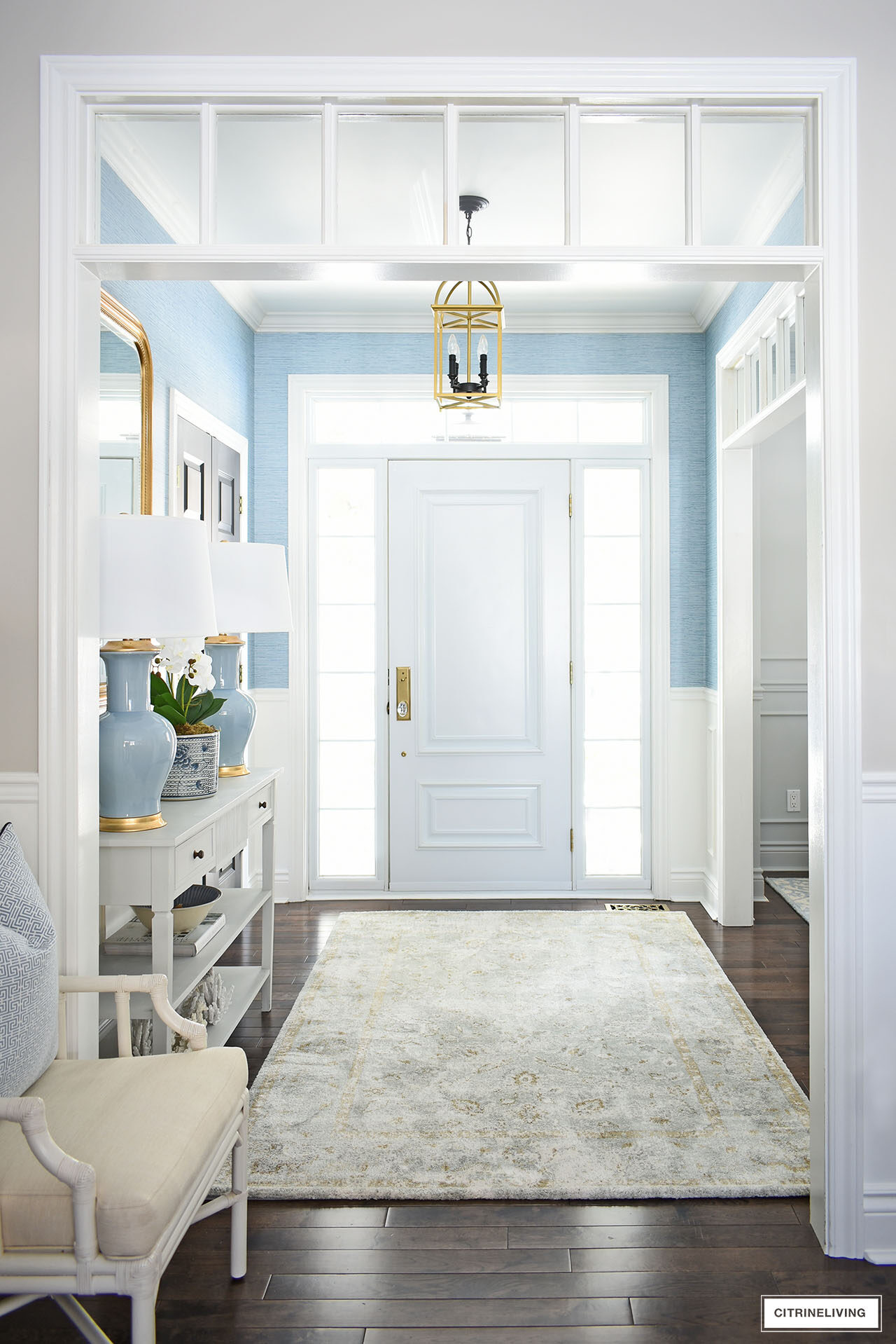 Entryway decorated for spring with blue lamps, gold mirror and a soft muted rug