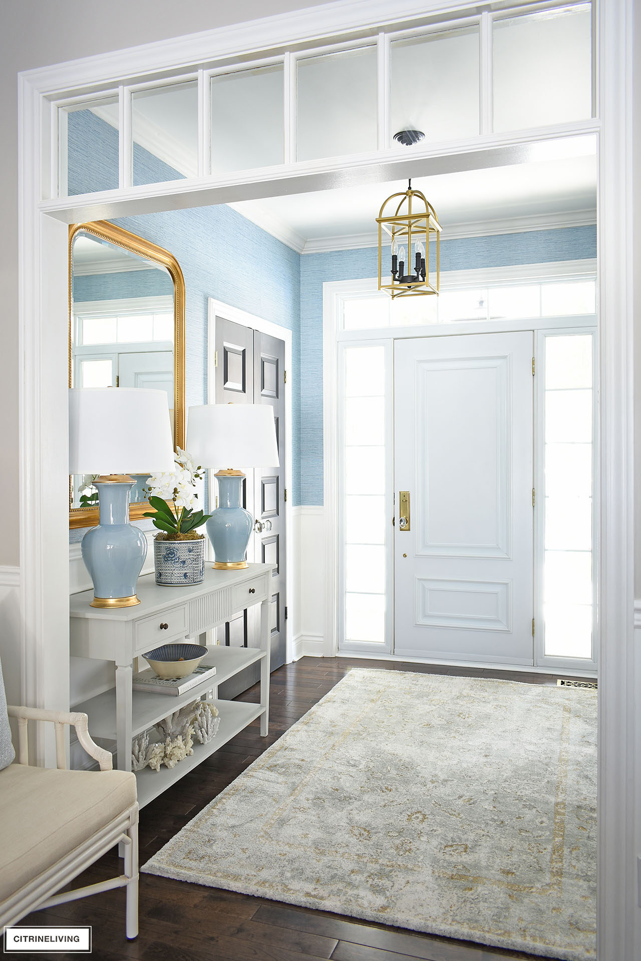 Entryway entryway console table styled for spring with a pair of blue lamps flanking an elegant orchid arrangement styled in front of a large gold mirror