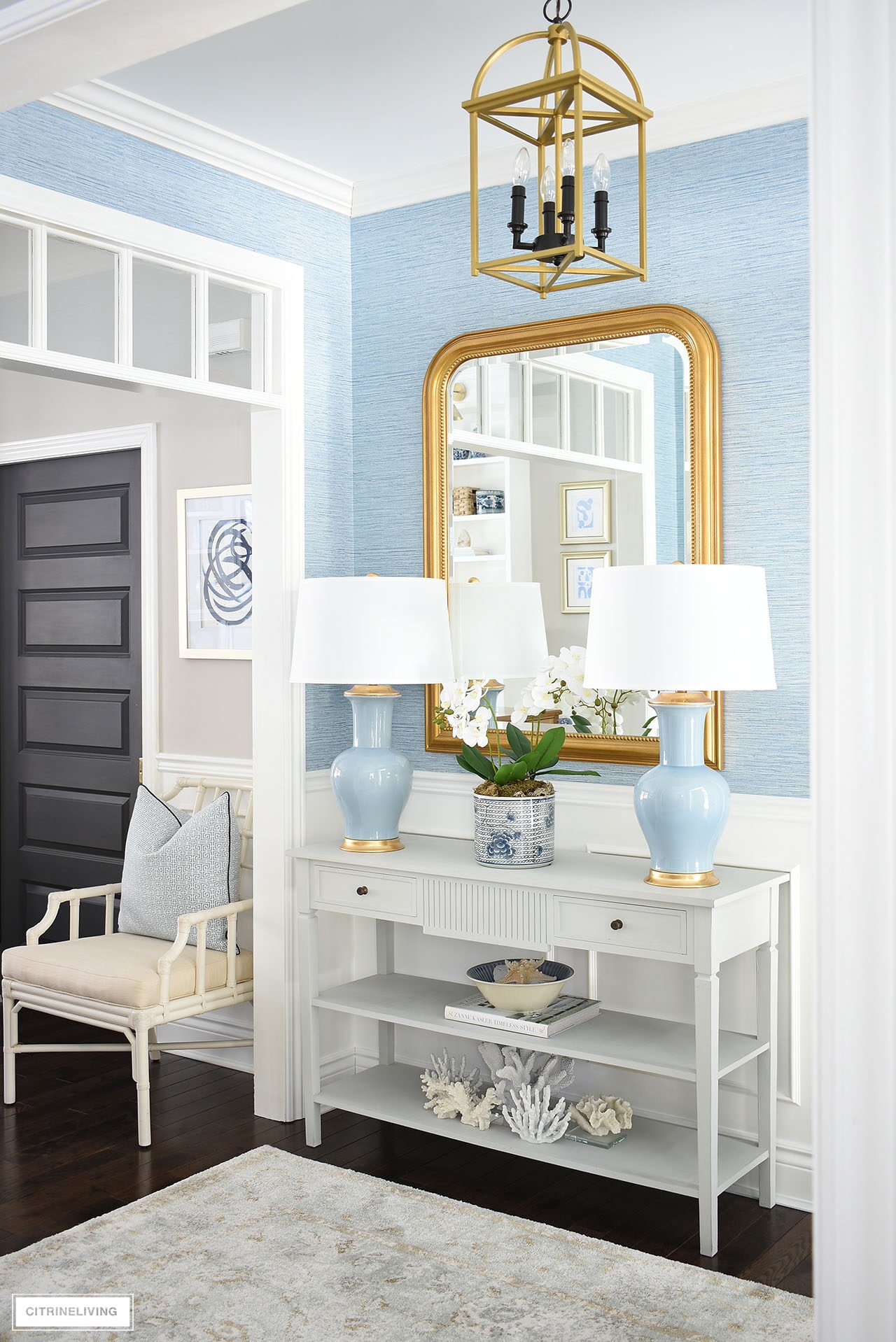 Entryway console table styled for spring with a pair of blue lamps flanking an elegant orchid arrangement styled in front of a large gold mirror