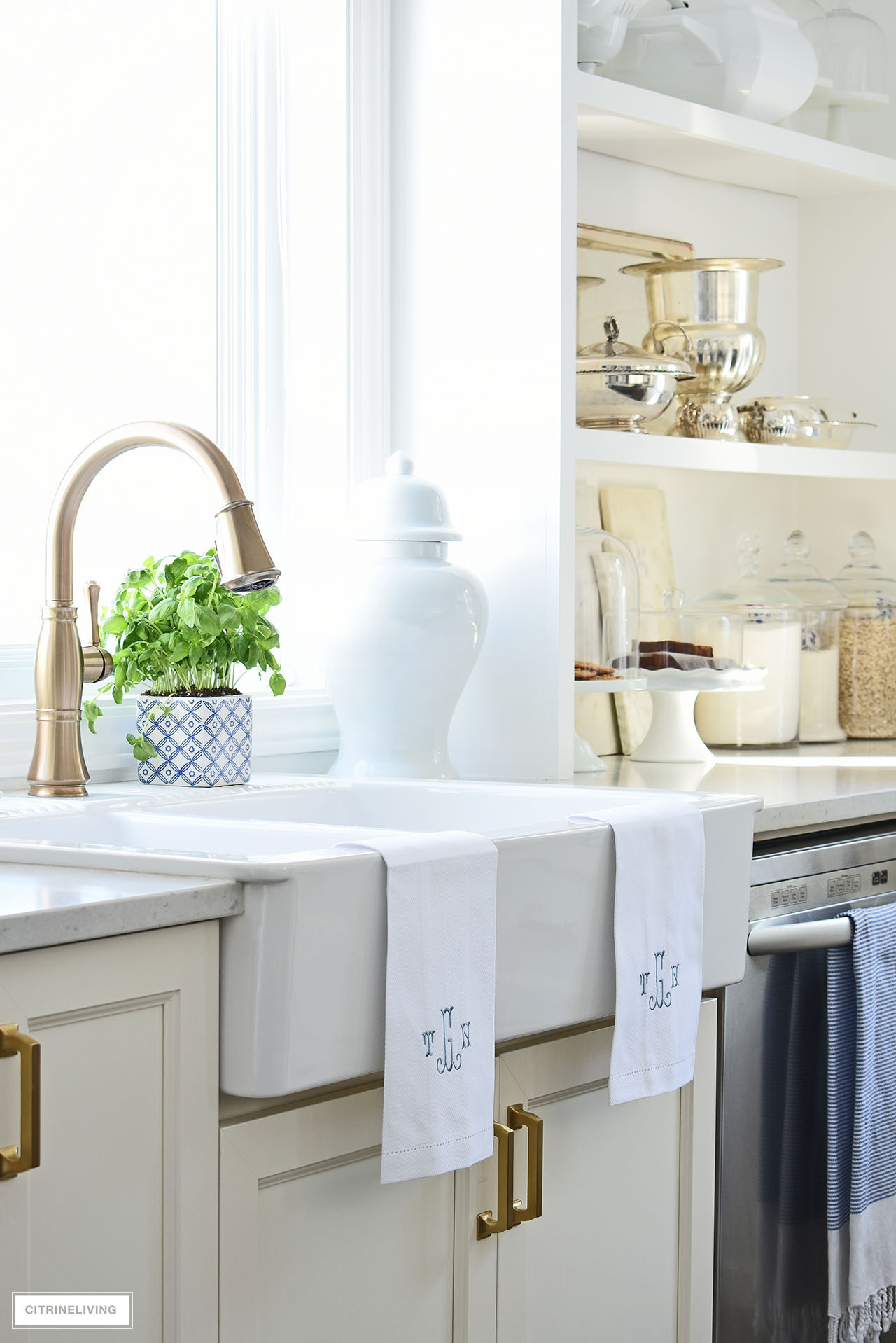 White kitchen farm sink with brass faucet and monogrammed towels.