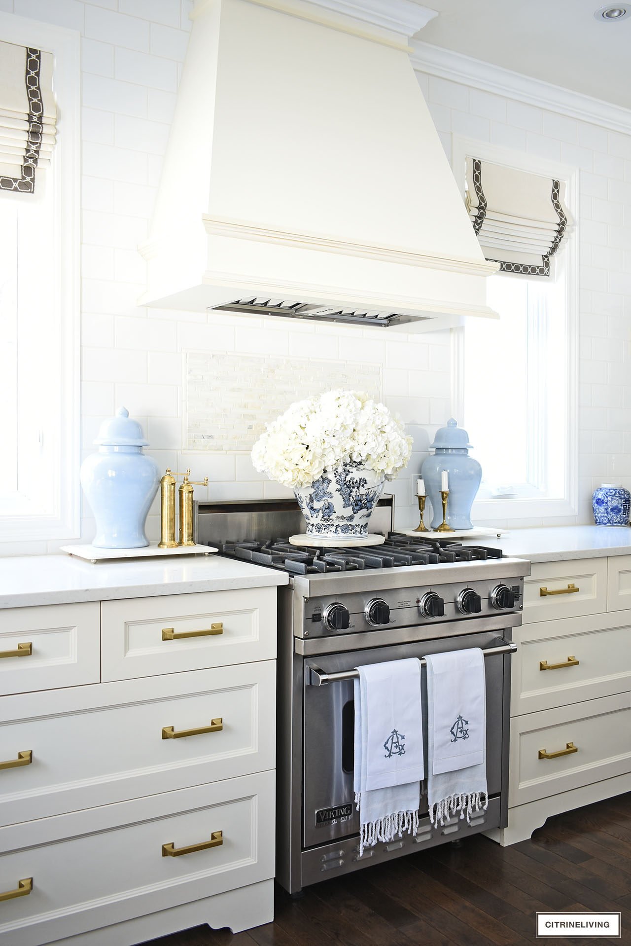 Elegant kitchen decorated for spring with blue and white ginger jars and an elegant orchid arrangement, light blue ginger jars flanking the stove with a beautiful large faux hydrangea arrangement on top.