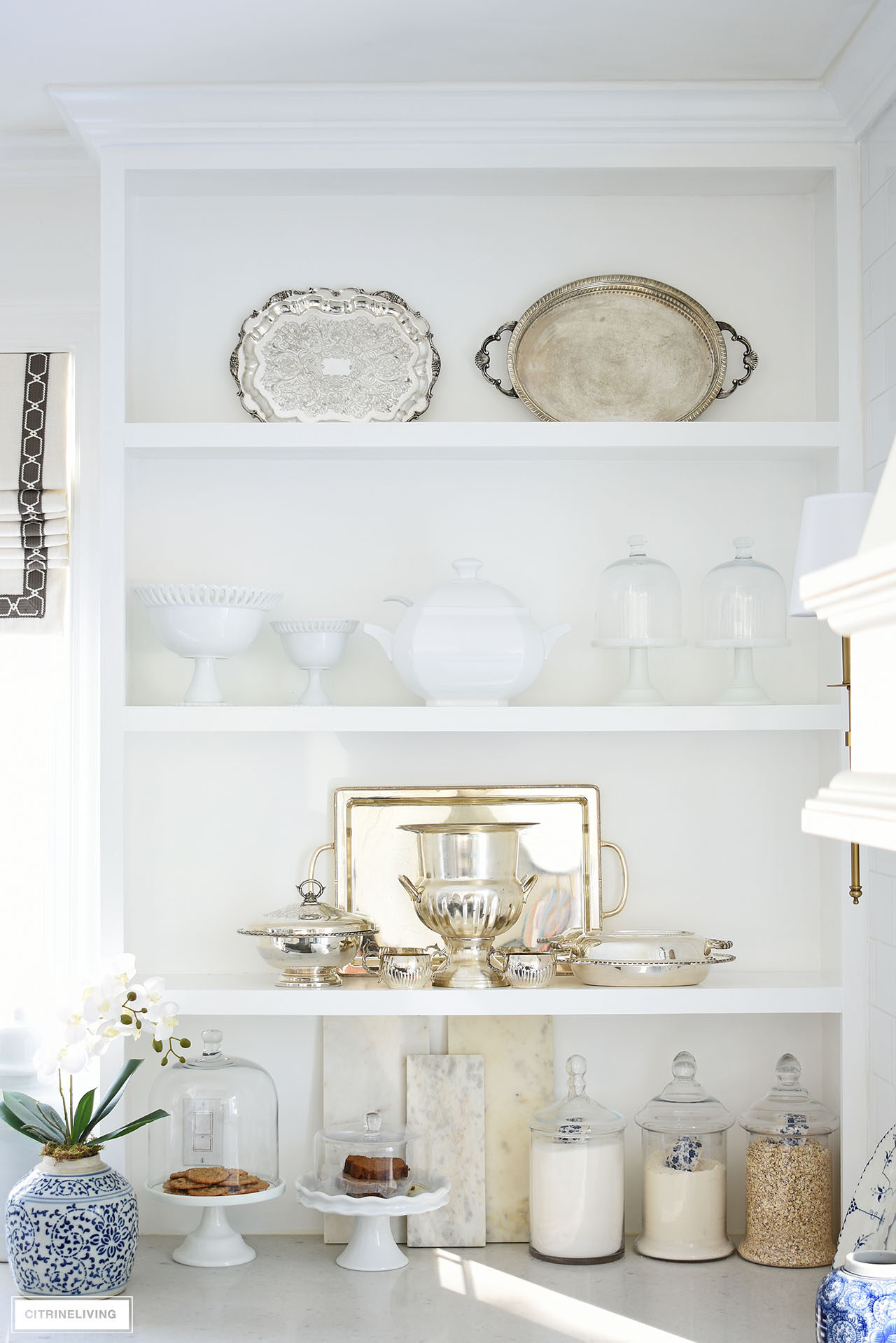 Traditional kitchen styled for spring with open shelves accessorized with silver serving pieces, white ceramics and glass apothecary canisters.