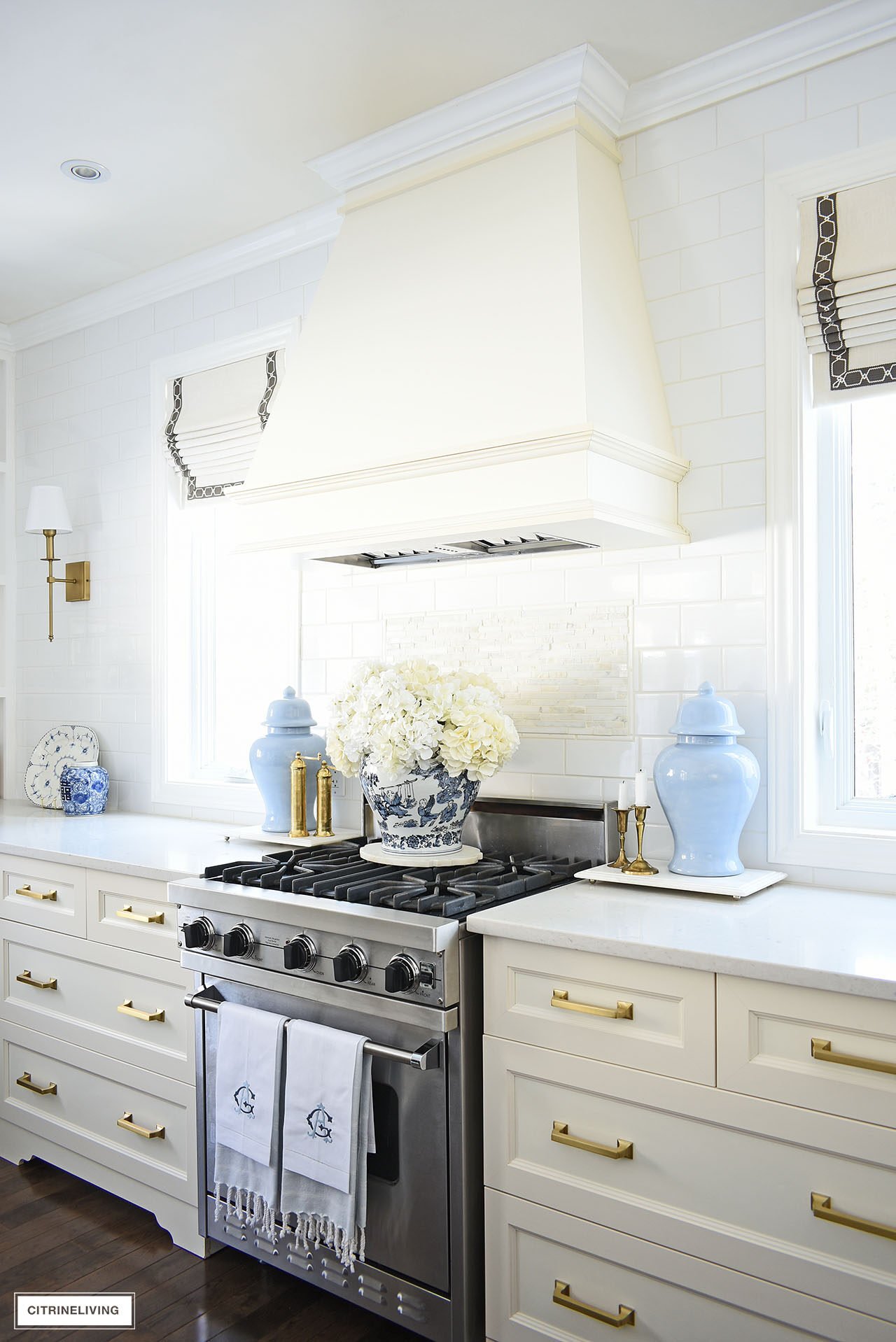 Classic kitchen decorated for spring with light blue ginger jars flanking the stove with a beautiful large faux hydrangea arrangement on top.