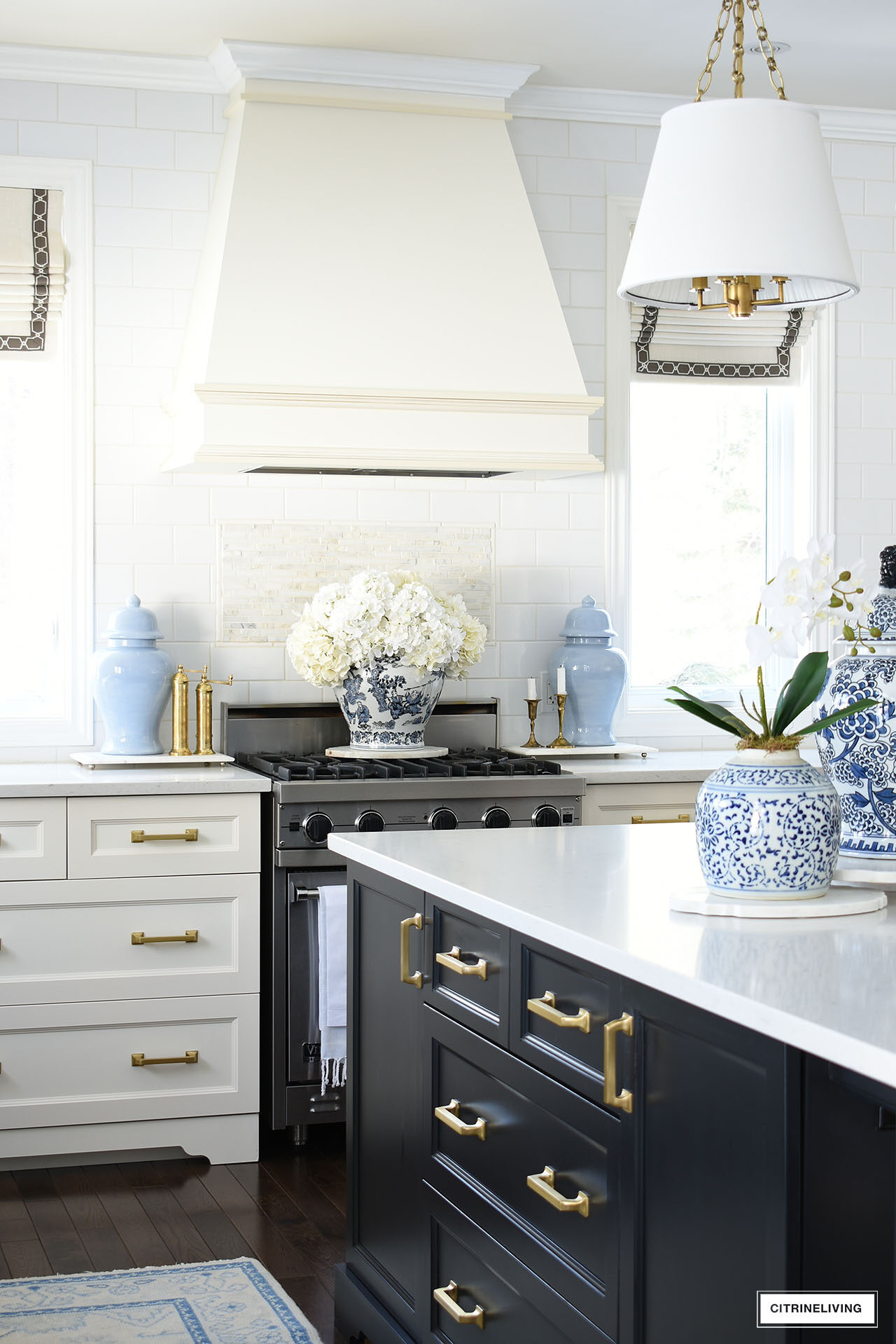 Elegant kitchen decorated for spring with blue and white ginger jars and an elegant orchid arrangement, light blue ginger jars flanking the stove with a beautiful large faux hydrangea arrangement on top.