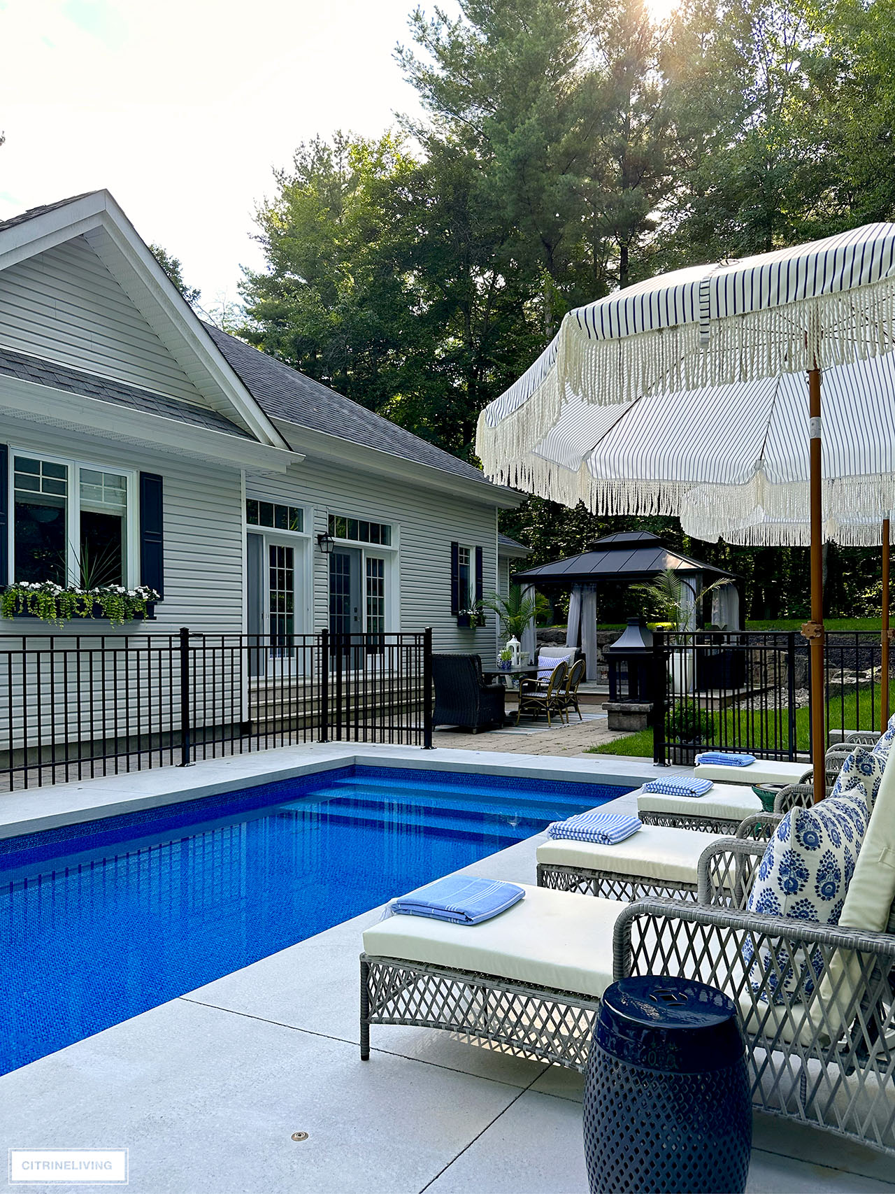Resort style in ground pool with loungers and umbrellas, facing the back elevation of a traditional, east coast style home.