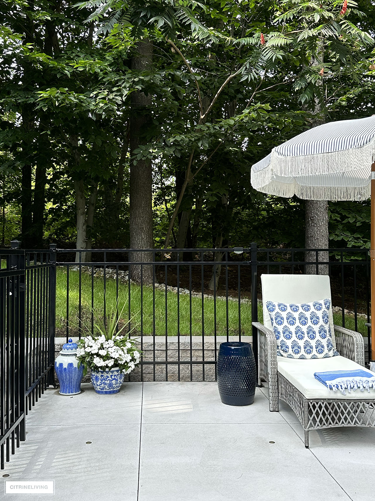 Corner of cement deck, styled with ginger jar and planter, lounger, umbrella and garden stool.