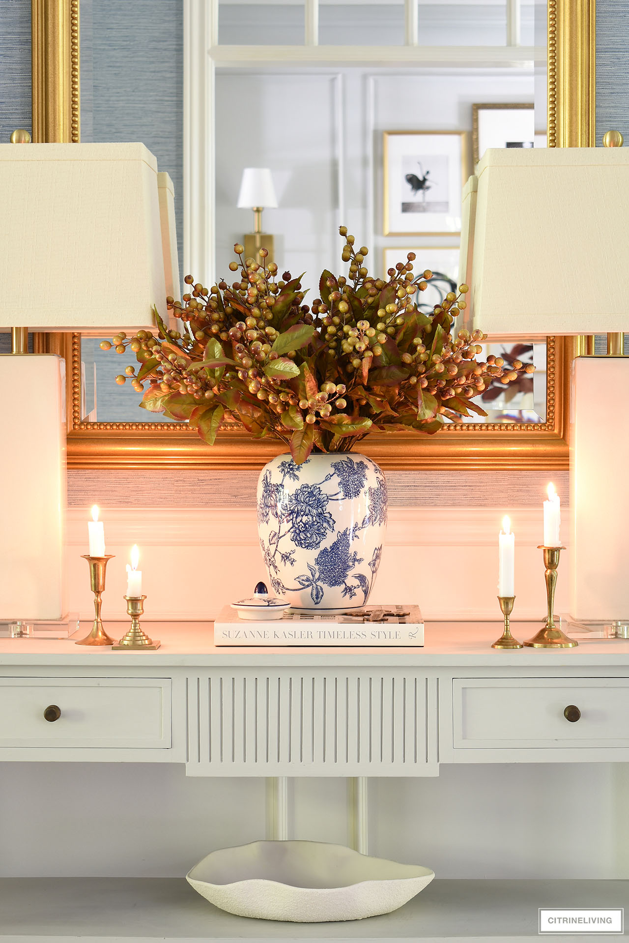 Elegant fall decor on a light grey console table - vintage gold candlesticks, blue and white jar with an autumn arrangement.
