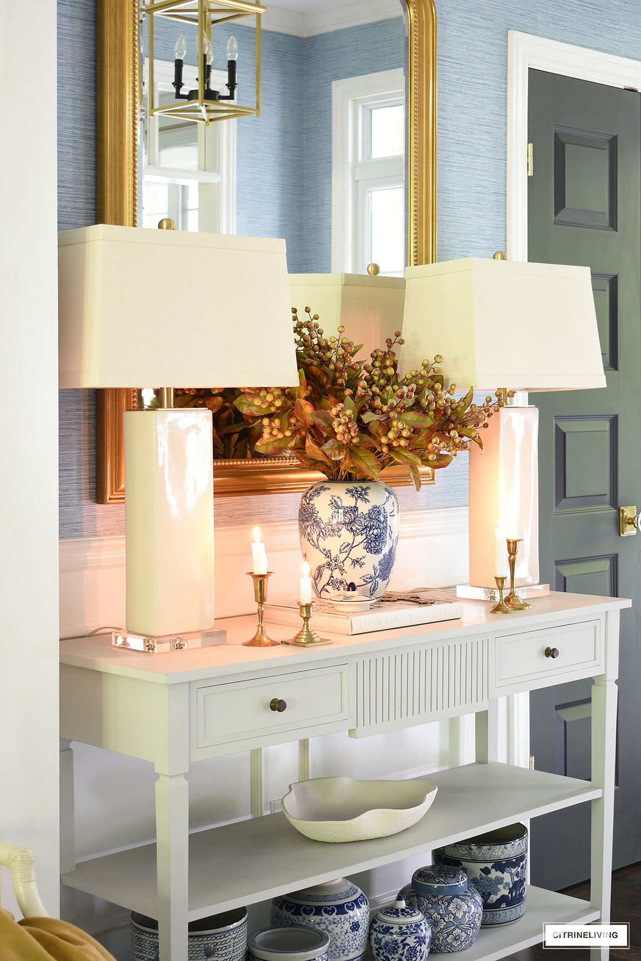 Ivory lamps flank a fall arrangement on a light grey console table.