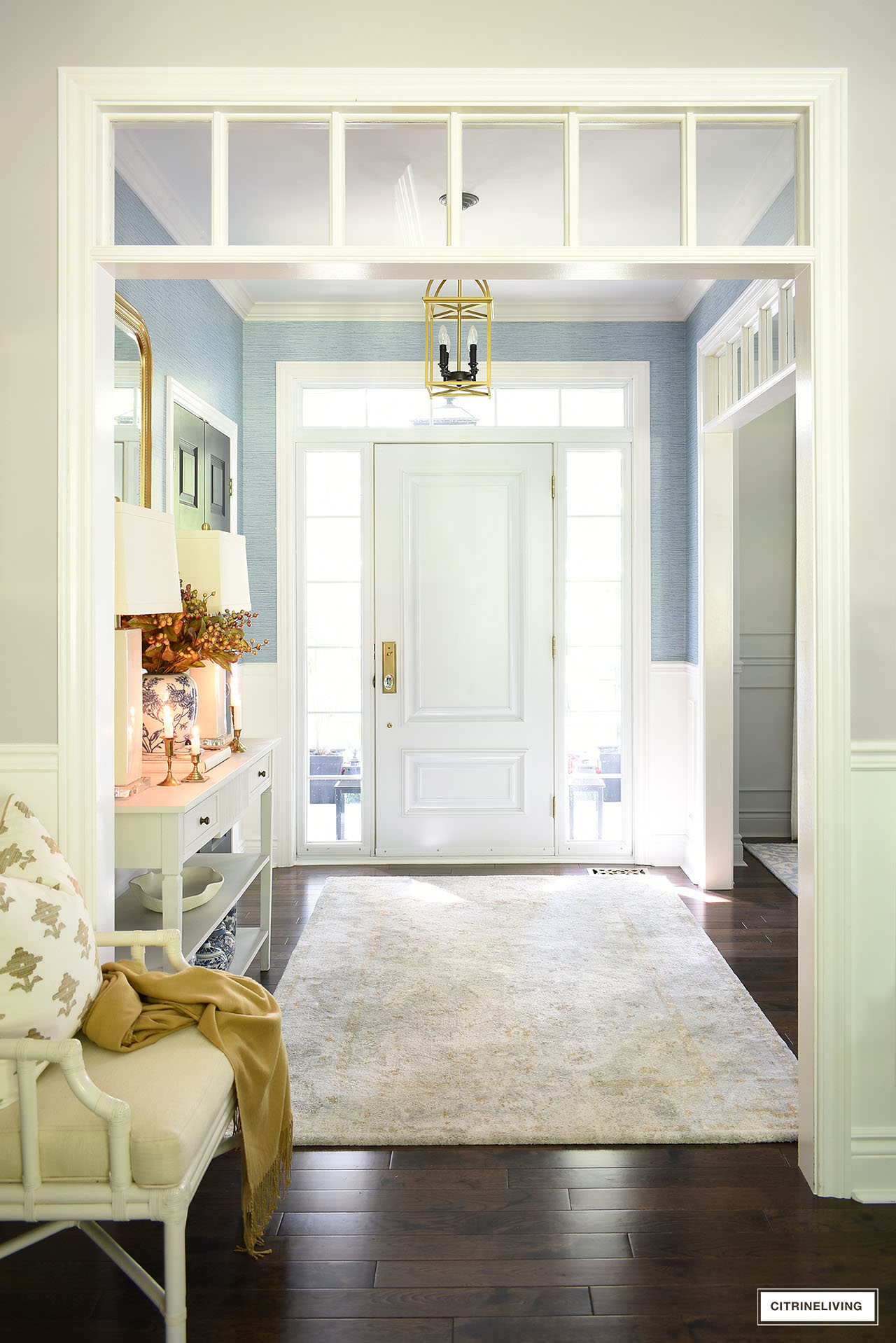 A chic entryway with blue grasscloth wallpaper, a simple light grey rug, accented with blue, ivory and gold.