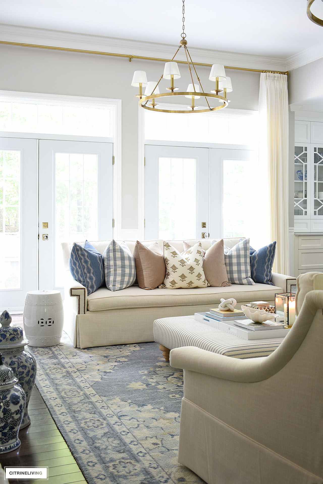 Ivory skirted sofa styled with luxe pillows in blue, tan and ivory in front of double french doors